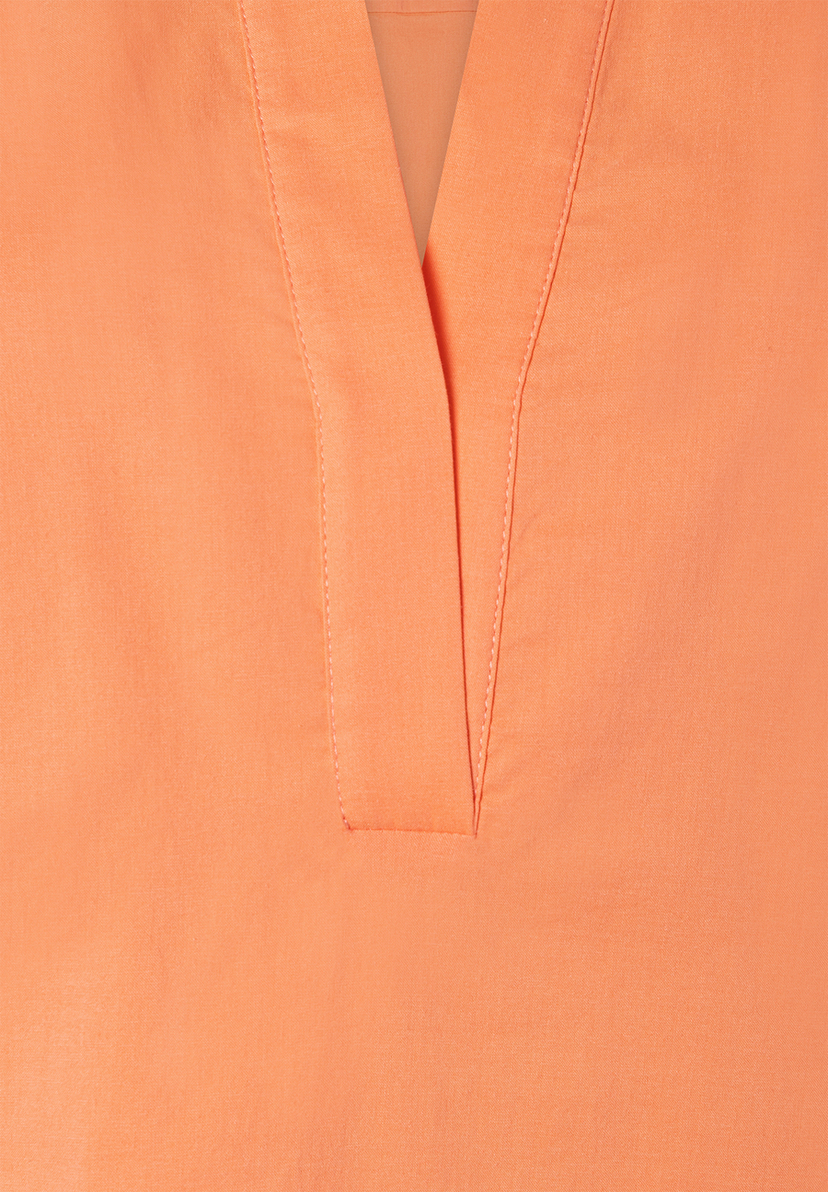 Detailaufnahme einer korallfarbenen Bluse von MORE & MORE aus Popeline mit V-Ausschnitt und sichtbaren Nähten.