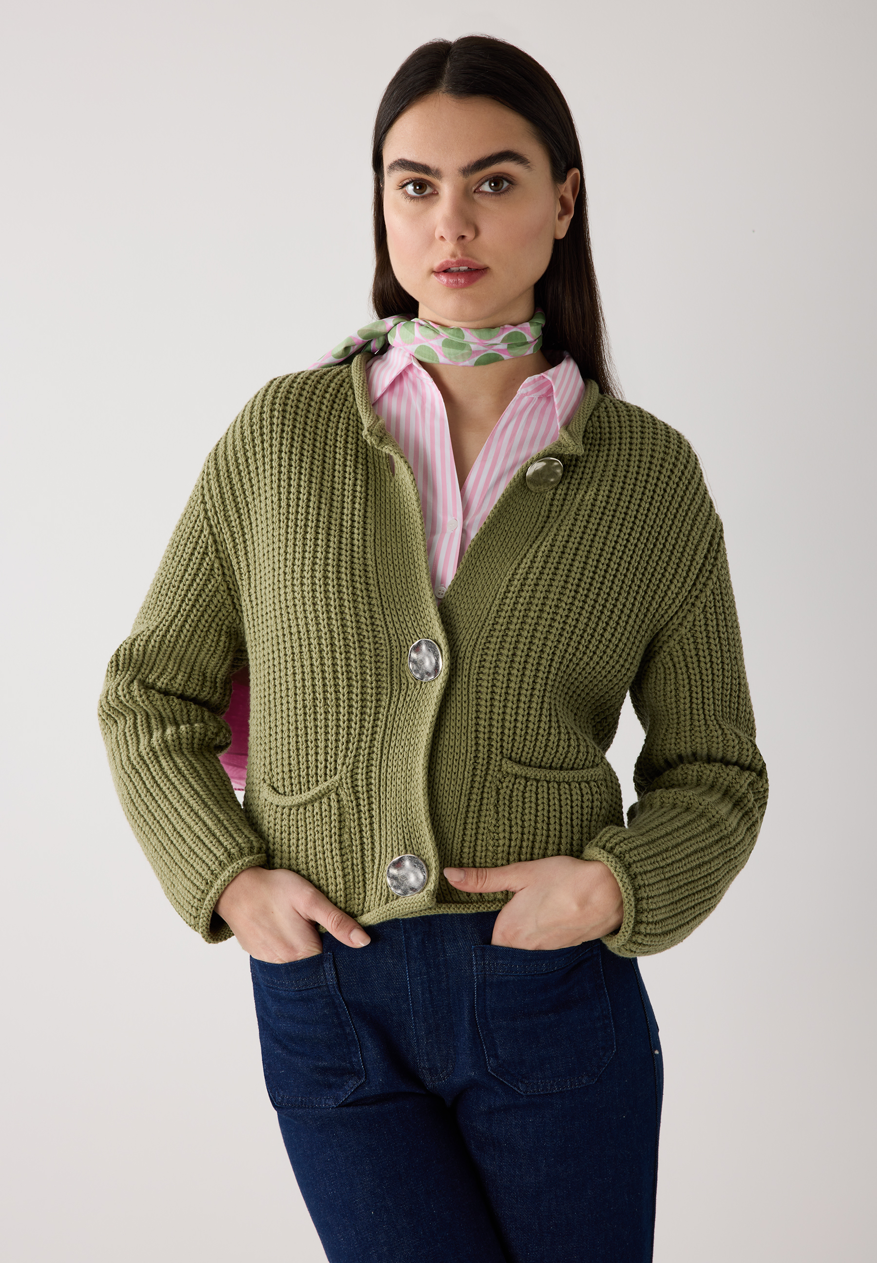 Eine Frau trägt einen olivgrünen Rippstrick-Cardigan von MORE & MORE über einem rosa gestreiften Hemd und einer gemusterten Halskette. Eine Frau trägt einen olivgrünen Rippstrick-Cardigan von MORE & MORE über einem rosa gestreiften Hemd und einer gemusterten Halskette.