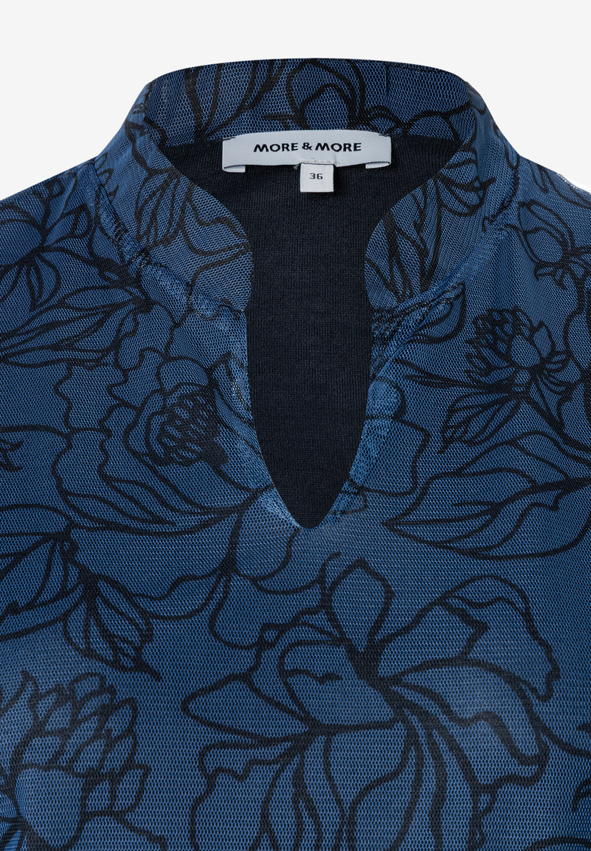 Nahaufnahme eines blauen MORE & MORE Mesh-Tops mit schwarzem Blumenmuster und V-Ausschnitt. Nahaufnahme eines blauen MORE & MORE Mesh-Tops mit schwarzem Blumenmuster und V-Ausschnitt.