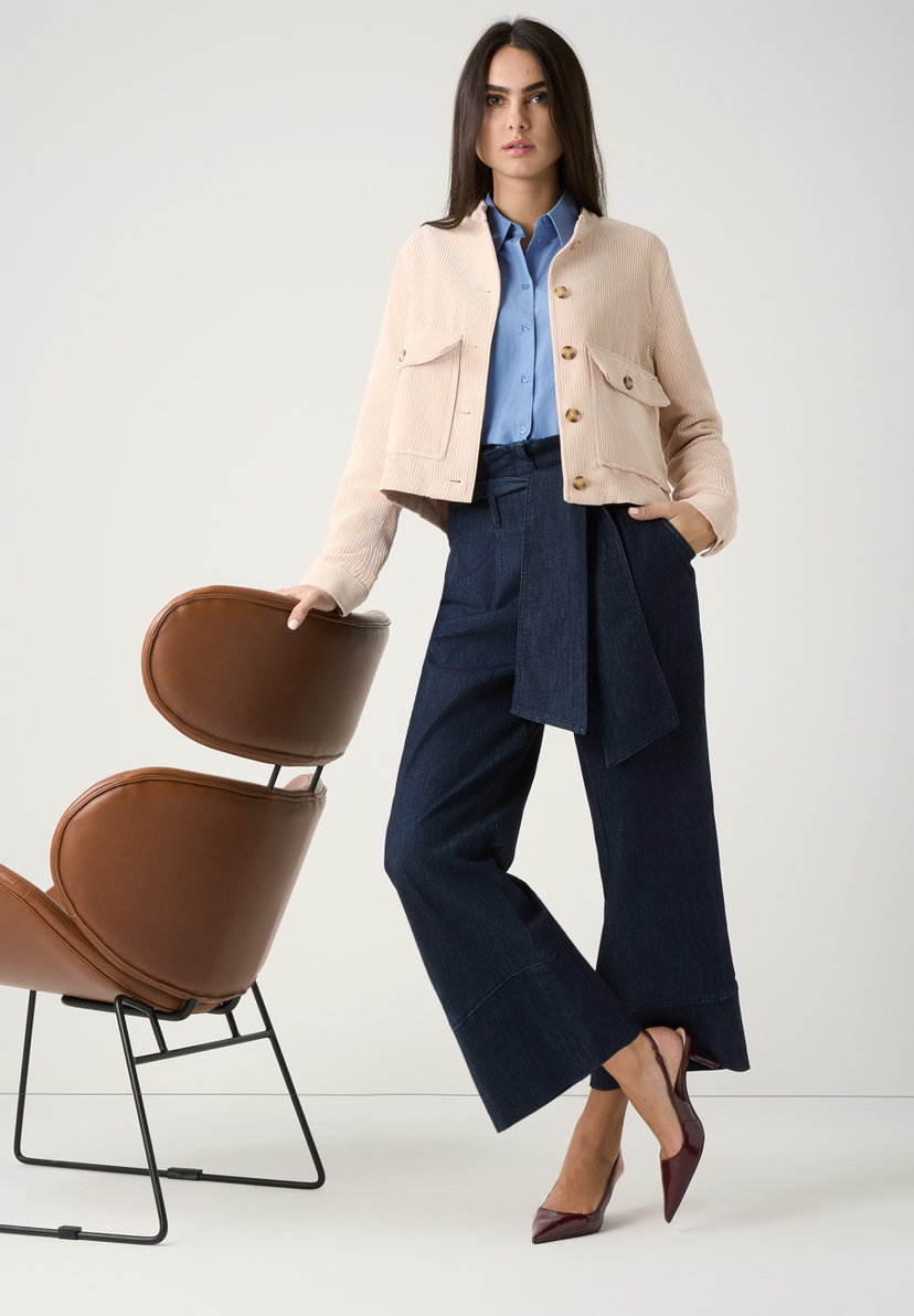 Eine Frau in MORE & MORE Oberteilen posiert lässig neben einem braunen Stuhl vor neutralem Hintergrund. Eine Frau in MORE & MORE Oberteilen posiert lässig neben einem braunen Stuhl vor neutralem Hintergrund.