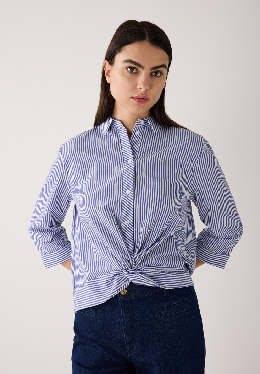 Eine Frau trägt eine blau-weiß gestreifte MORE & MORE Bluse mit Knoten und Jeans. Eine Frau trägt eine blau-weiß gestreifte MORE & MORE Bluse mit Knoten und Jeans.