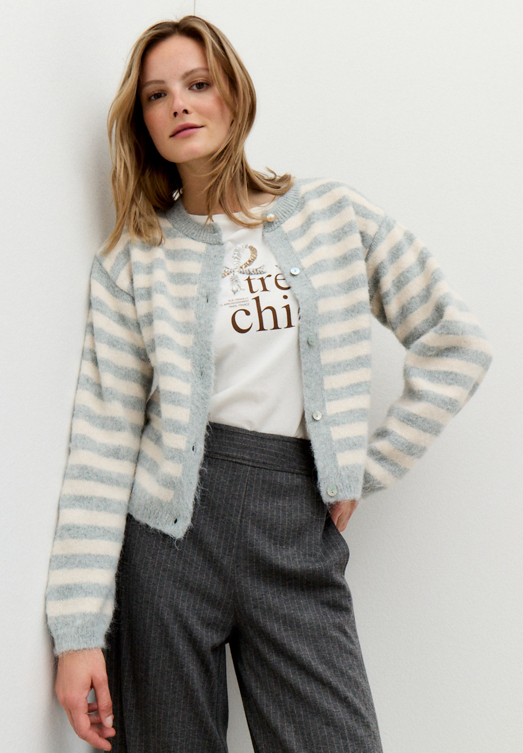 Eine Frau, die einen MORE & MORE Cardigan mit grauen Streifen über einem T-Shirt mit Aufdruck trägt.