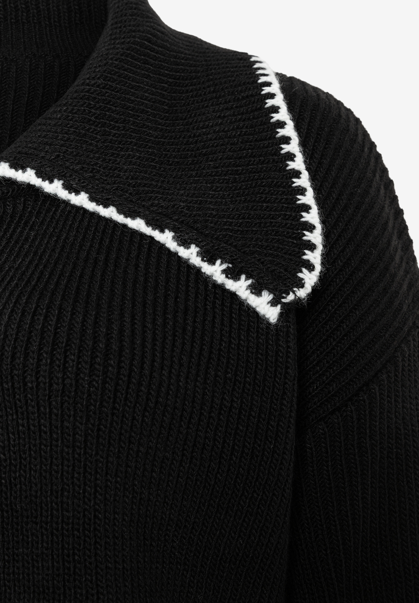 Detailansicht eines schwarzen Strick-Oberteils von MORE & MORE mit weißer Kontrastnaht am Kragen. Detailansicht eines schwarzen Strick-Oberteils von MORE & MORE mit weißer Kontrastnaht am Kragen.