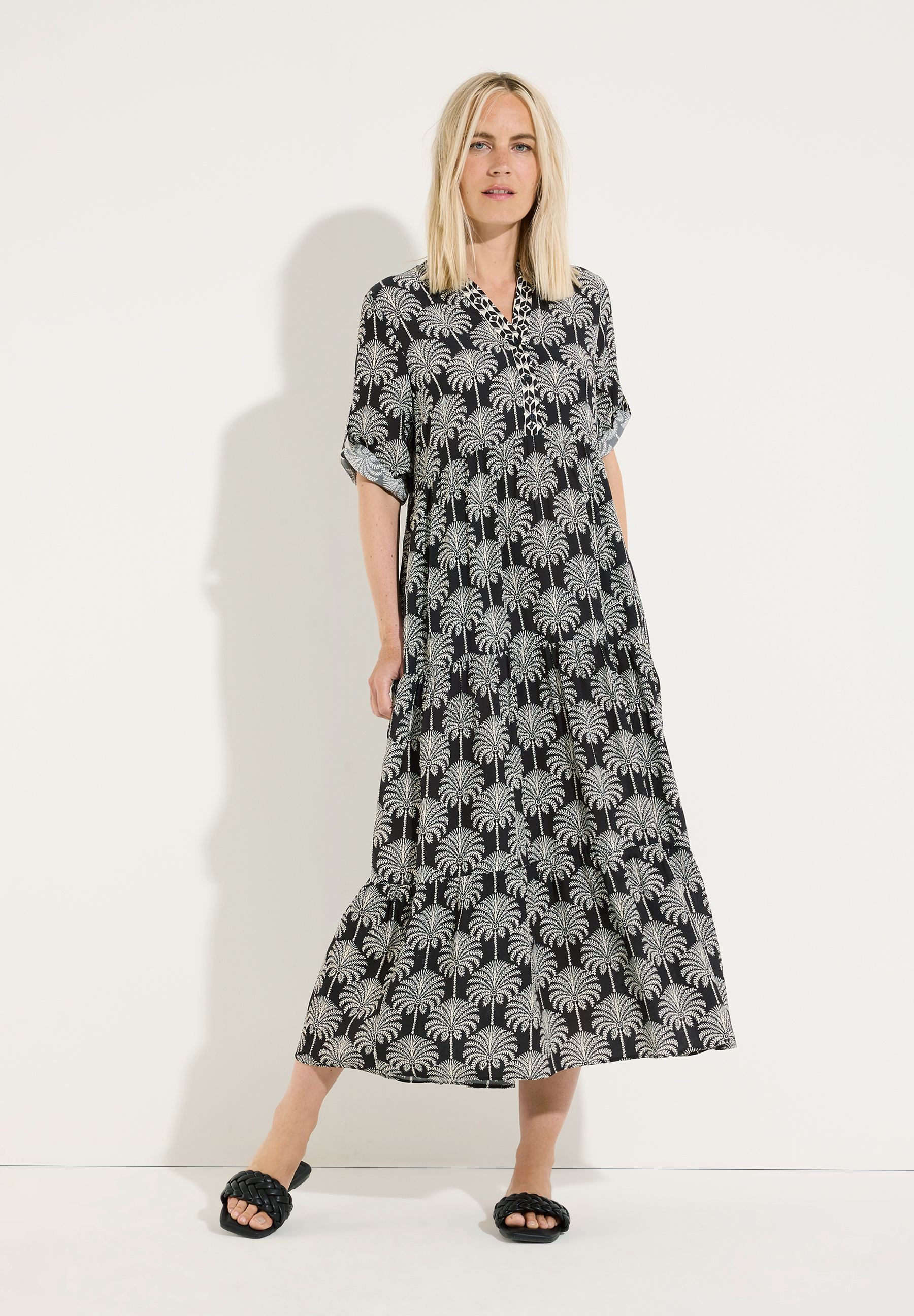 MORE & MORE Midi-Kleid mit Palmenmuster in Schwarz. Eine Frau trägt das schwarze Kleid mit weitem Rock und kurzen Ärmeln.