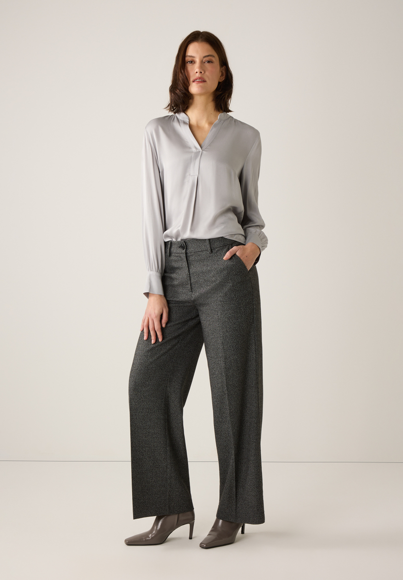 Eine Frau in MORE & MORE Hose und Bluse posiert vor einem hellen Hintergrund. Eine Frau in MORE & MORE Hose und Bluse posiert vor einem hellen Hintergrund.