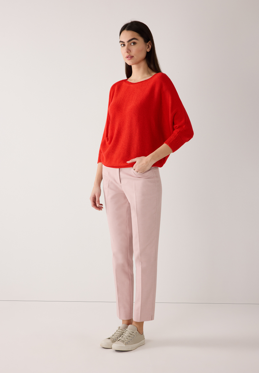 Eine Frau in MORE & MORE Strickware, roter Pullover mit rosa Hose und Turnschuhen vor weißem Hintergrund. Eine Frau in MORE & MORE Strickware, roter Pullover mit rosa Hose und Turnschuhen vor weißem Hintergrund.