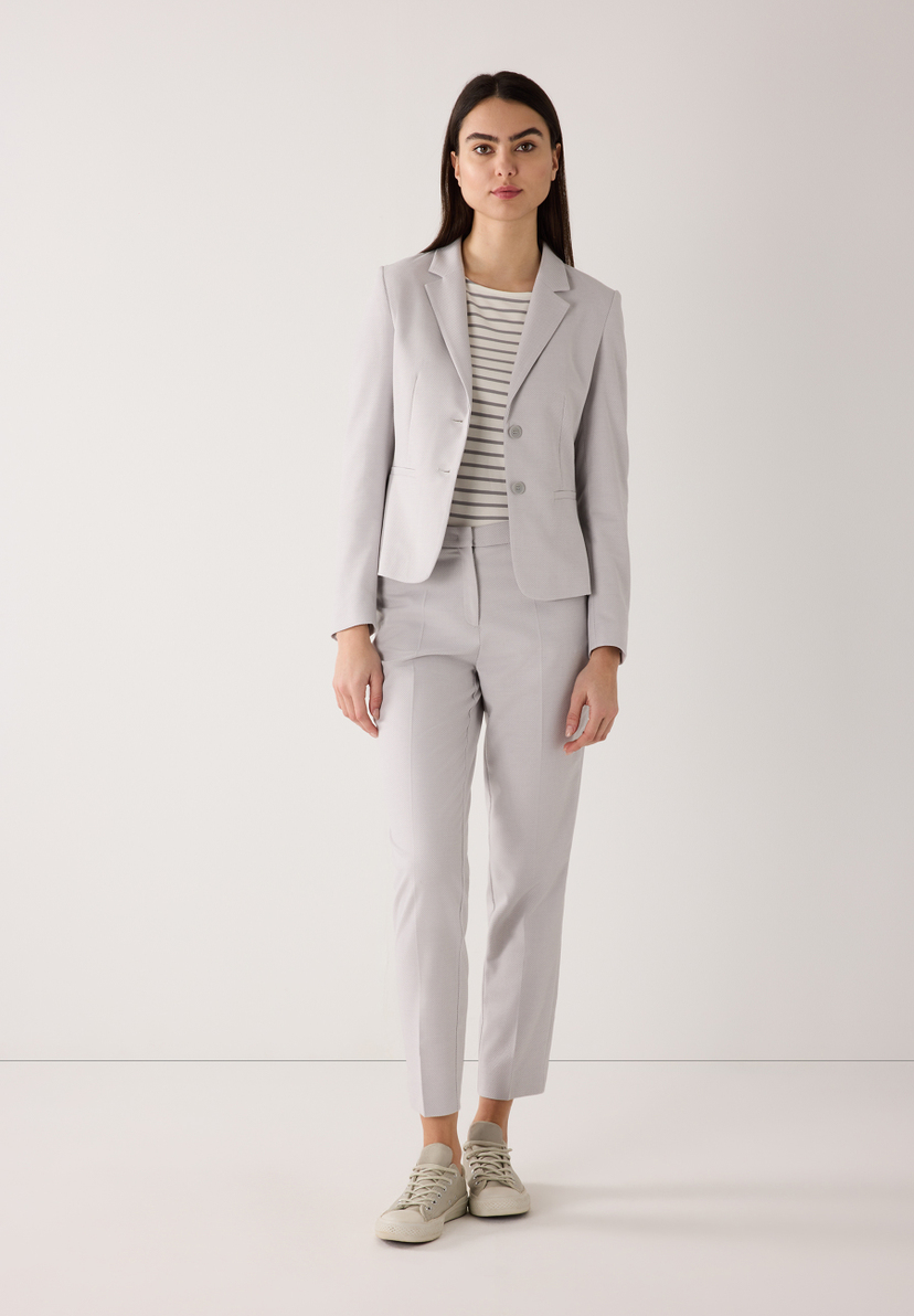 Eine Frau trägt ein graues MORE & MORE Blazer-Outfit mit einem gestreiften Oberteil und Sneakers vor einem weißen Hintergrund. Eine Frau trägt ein graues MORE & MORE Blazer-Outfit mit einem gestreiften Oberteil und Sneakers vor einem weißen Hintergrund.