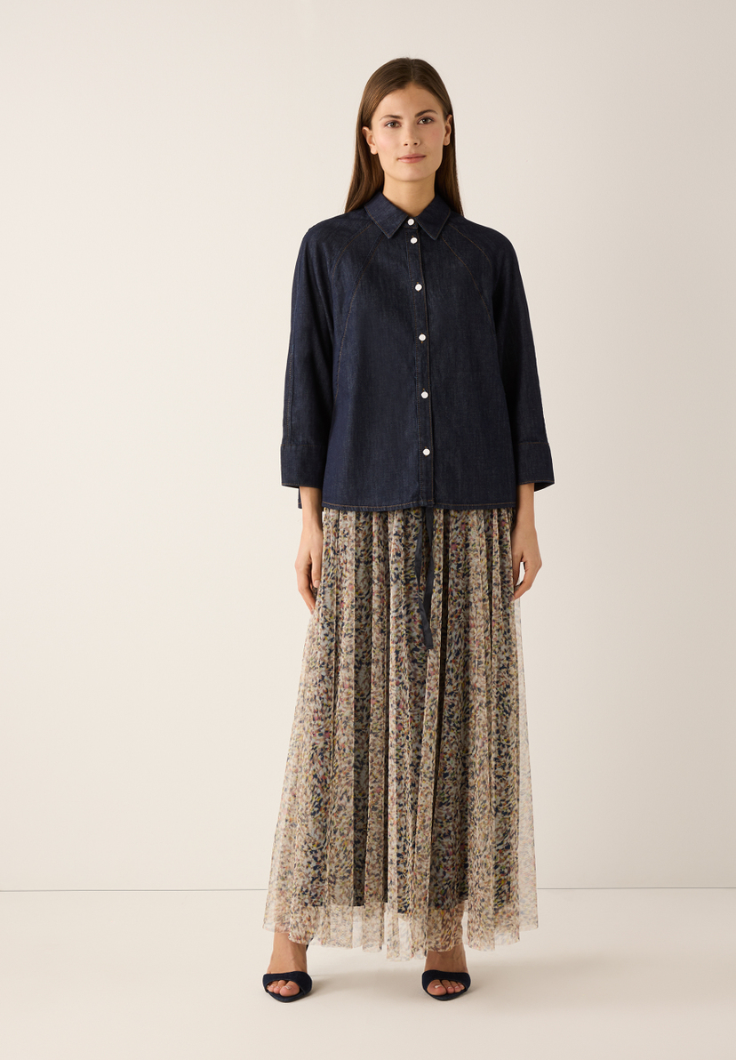 Eine Frau trägt eine MORE & MORE Bluse aus Jeansstoff und einen langen, plissierten Rock mit Blumenmuster. Eine Frau trägt eine MORE & MORE Bluse aus Jeansstoff und einen langen, plissierten Rock mit Blumenmuster.