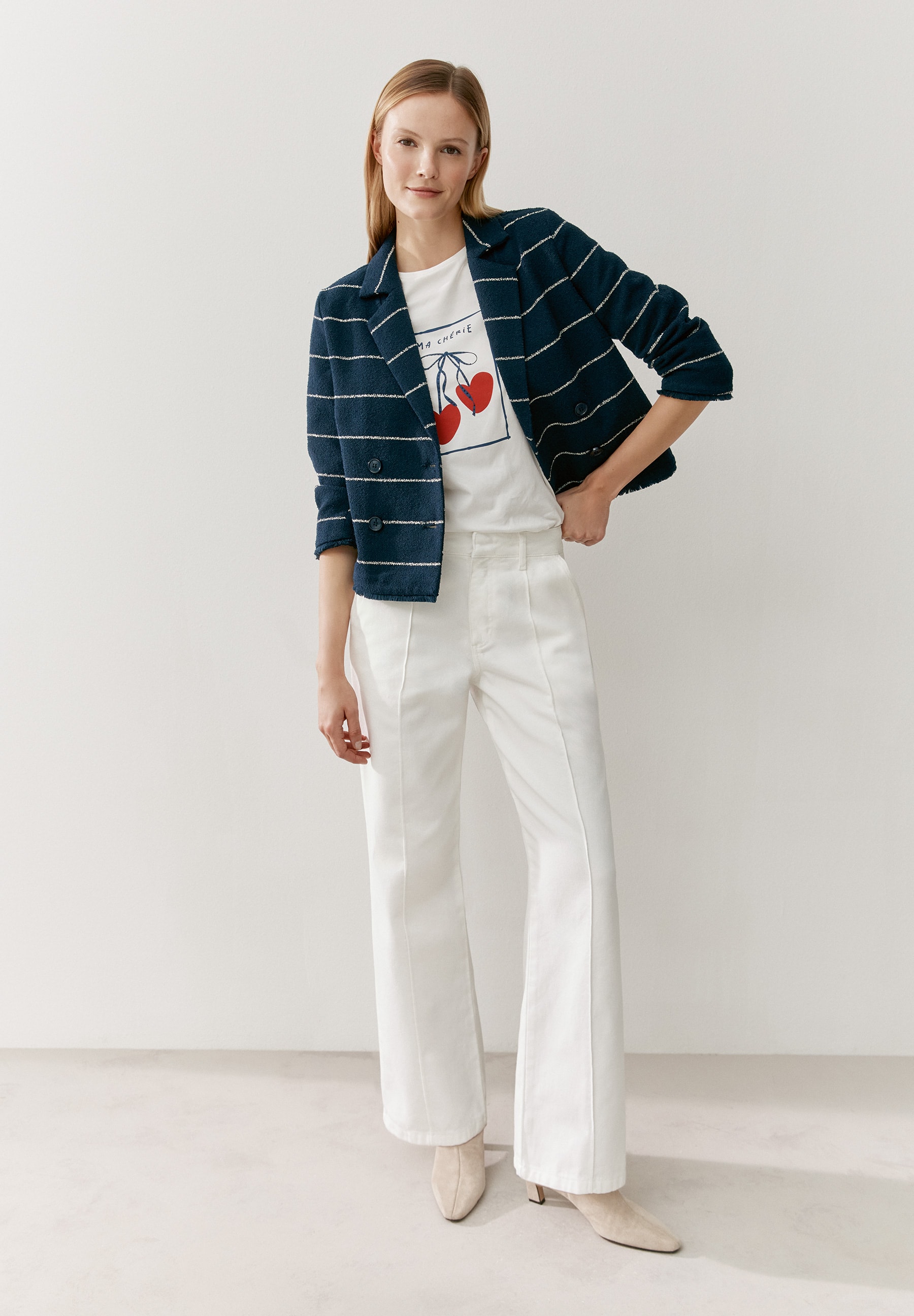 Eine Frau trägt ein MORE & MORE T-Shirt/Top mit Kirschen unter einem gestreiften Blazer und einer weißen Hose vor einem weißen Hintergrund. Eine Frau trägt ein MORE & MORE T-Shirt/Top mit Kirschen unter einem gestreiften Blazer und einer weißen Hose vor einem weißen Hintergrund.
