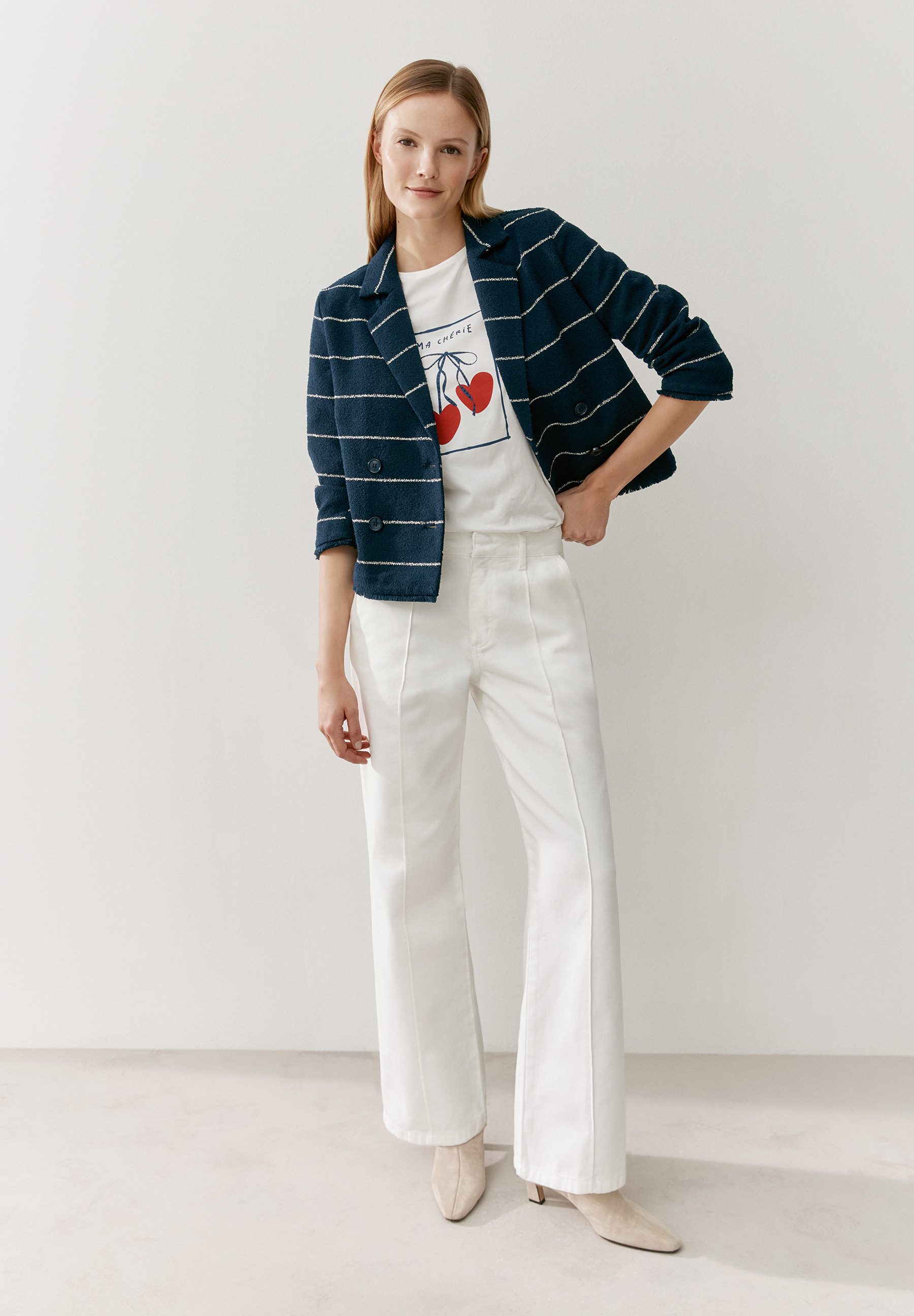 Eine Frau trägt ein MORE & MORE T-Shirt/Top mit Kirschen unter einem gestreiften Blazer und einer weißen Hose vor einem weißen Hintergrund. Eine Frau trägt ein MORE & MORE T-Shirt/Top mit Kirschen unter einem gestreiften Blazer und einer weißen Hose vor einem weißen Hintergrund.