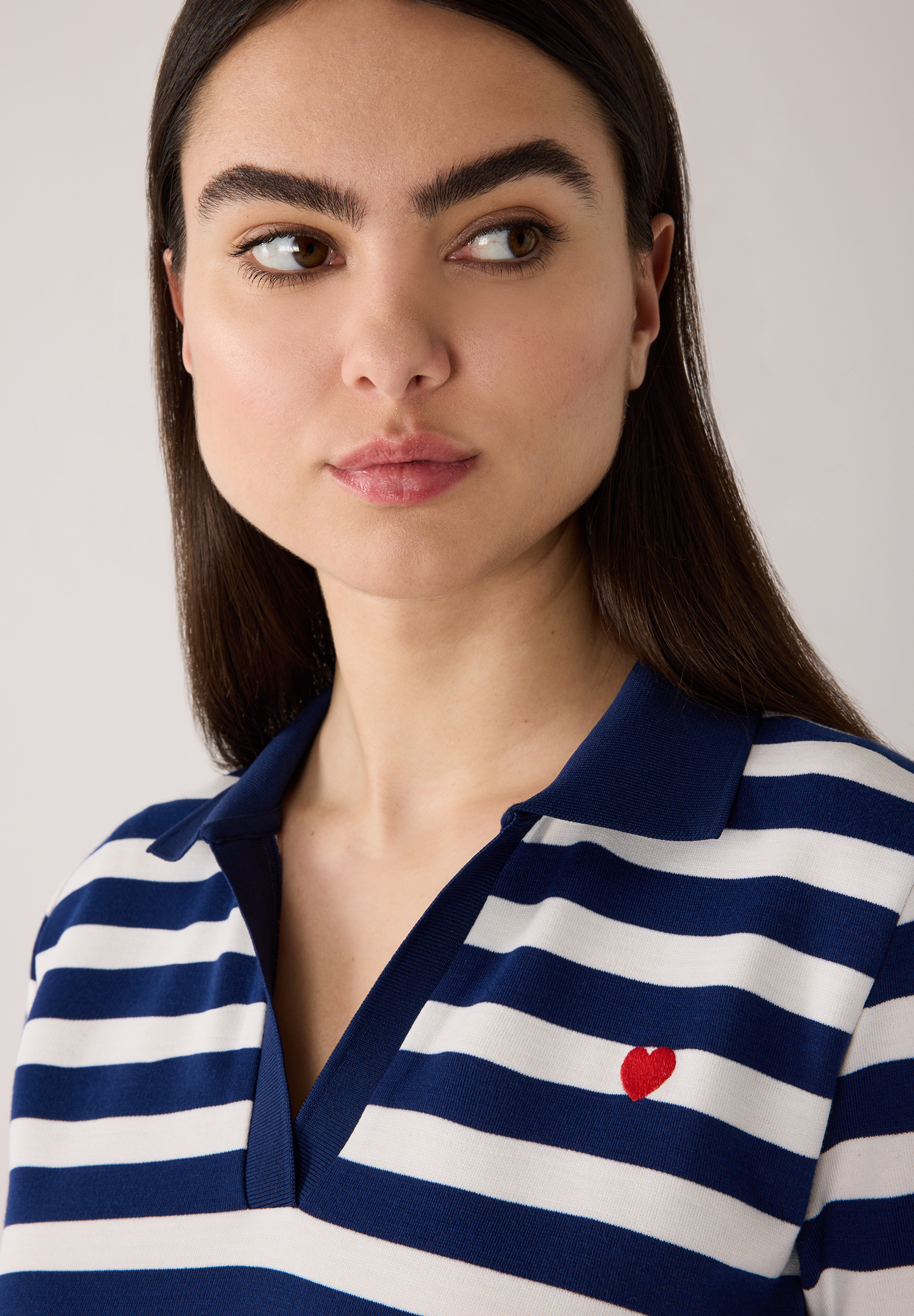 Eine Frau, die ein gestreiftes MORE & MORE Jersey-Oberteil mit einem kleinen roten Herz trägt. Eine Frau, die ein gestreiftes MORE & MORE Jersey-Oberteil mit einem kleinen roten Herz trägt.