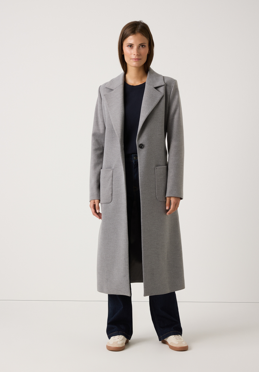 Eine Frau trägt einen langen, grauen MORE & MORE Mantel. Webware mit angenehmem Tragekomfort. Lässig offen mit Taschen. Eine Frau trägt einen langen, grauen MORE & MORE Mantel. Webware mit angenehmem Tragekomfort. Lässig offen mit Taschen.