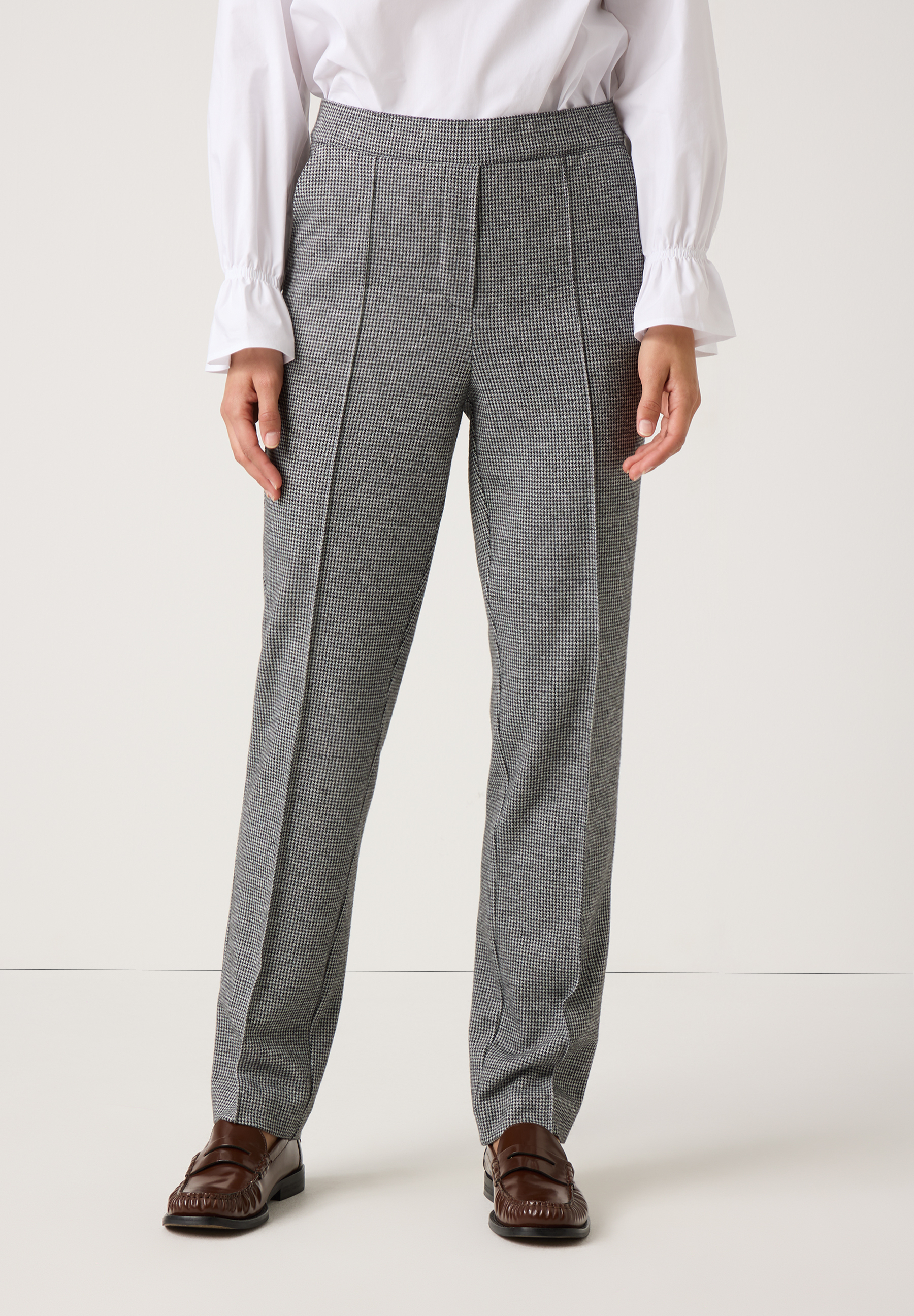 Eine Person, die eine MORE & MORE Hose mit Hahnentrittmuster und braune Schuhe vor einem weißen Hintergrund trägt.