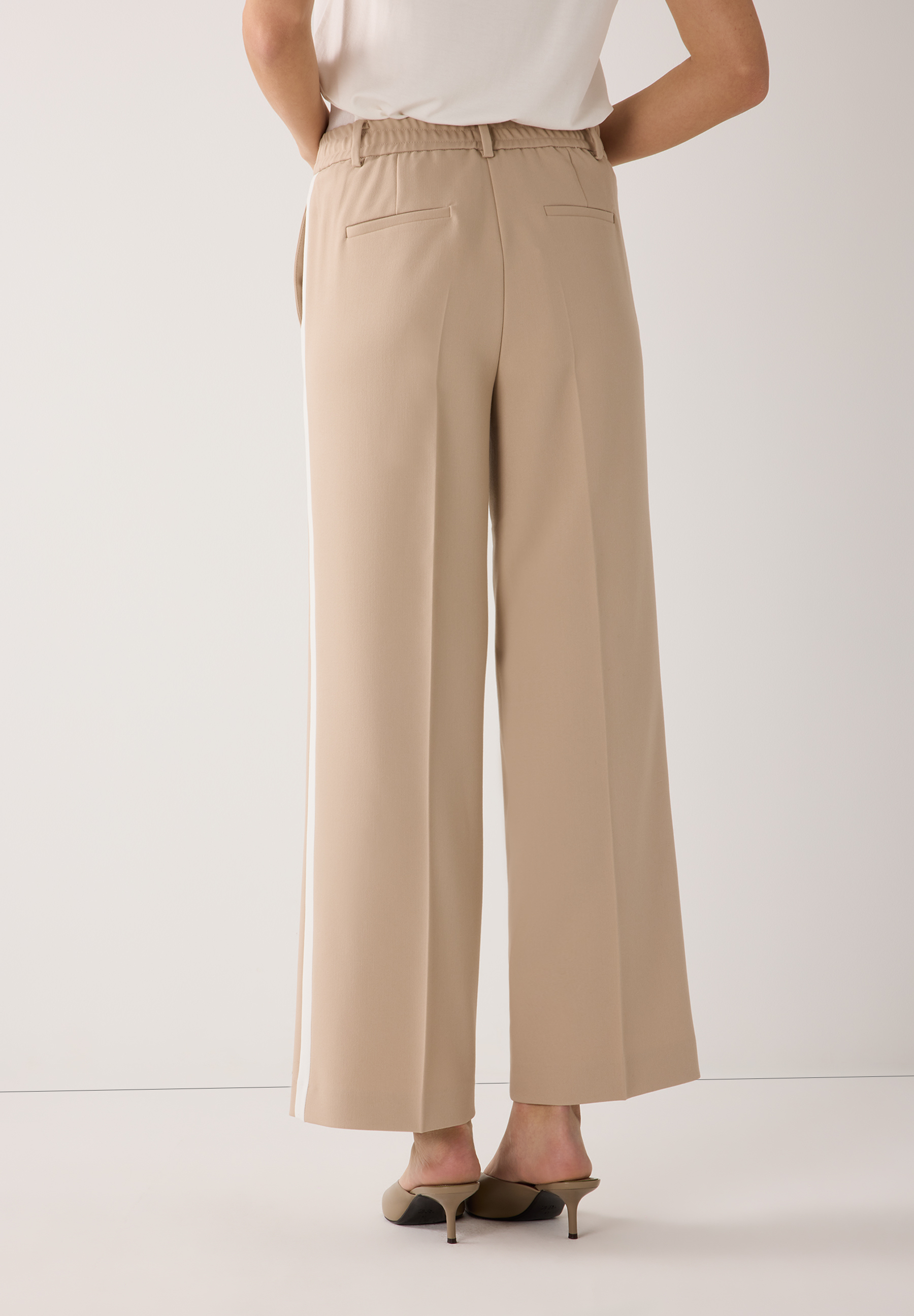 Eine beigefarbene MORE & MORE Hose mit breitem, geradem Bein und weißem Seitenstreifen. Eine beigefarbene MORE & MORE Hose mit breitem, geradem Bein und weißem Seitenstreifen.