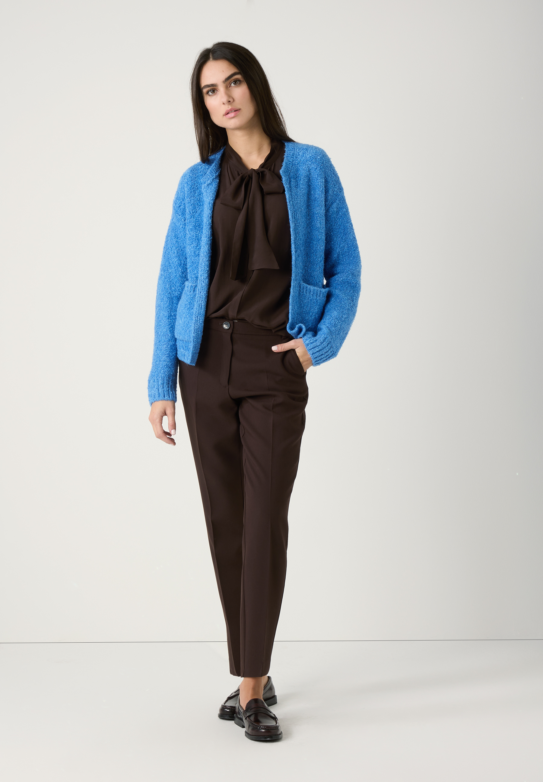 Eine Frau im MORE & MORE Strick-Bouclé-Look: blaue Strickjacke, braune Bluse mit Schleife, Hose und Schuhe. Komfortabler, warmer Griff. Eine Frau im MORE & MORE Strick-Bouclé-Look: blaue Strickjacke, braune Bluse mit Schleife, Hose und Schuhe. Komfortabler, warmer Griff.