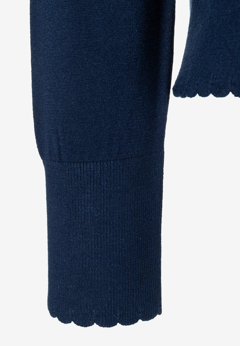 MORE & MORE dunkelblauer Pullover-Ärmel mit Rüschenmanschette und Wellensaum, Detailansicht auf beigem Hintergrund MORE & MORE dunkelblauer Pullover-Ärmel mit Rüschenmanschette und Wellensaum, Detailansicht auf beigem Hintergrund