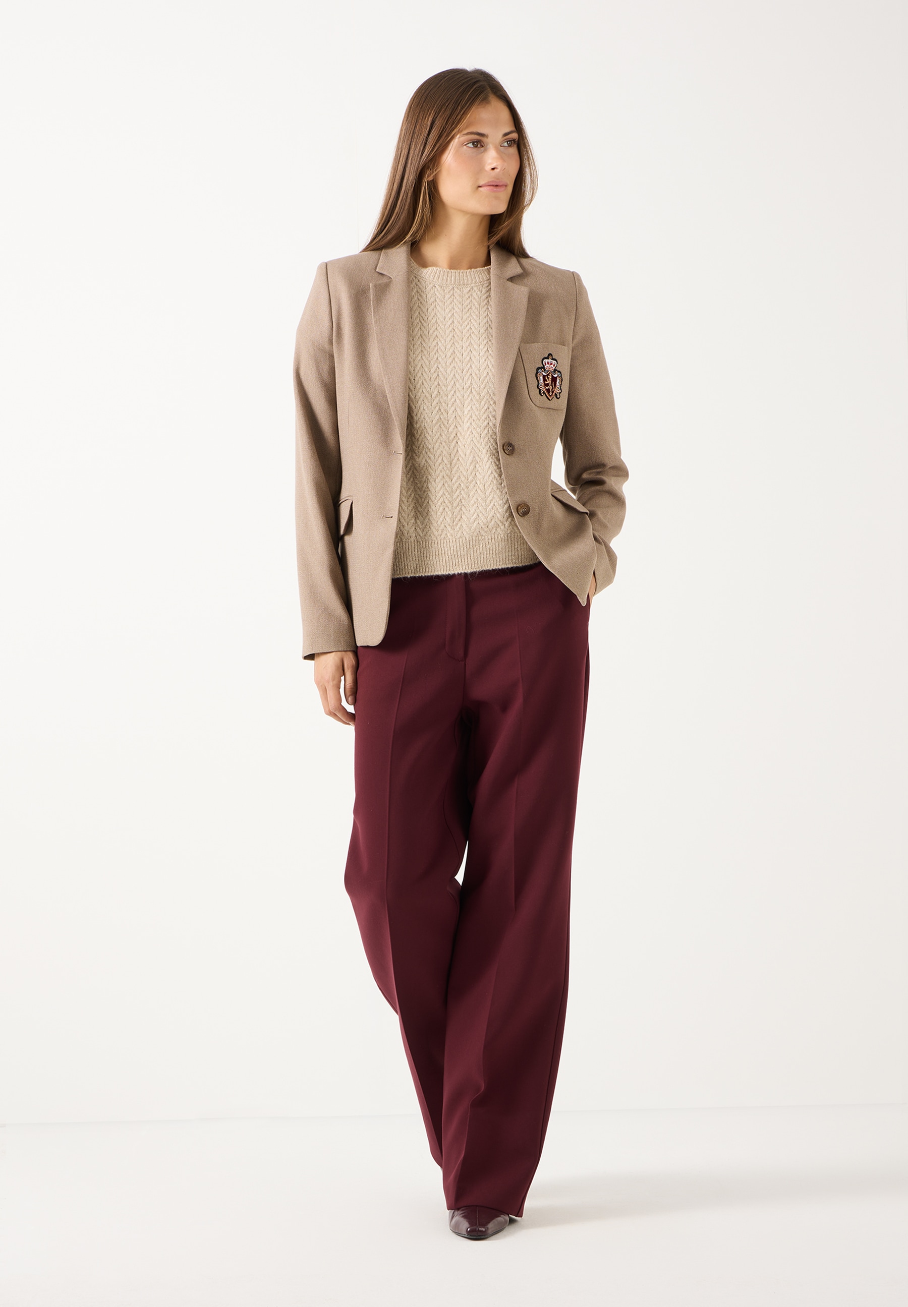 MORE & MORE Jeans: Stilvolle kastanienbraune Hose, kombiniert mit einem beigen Pullover und einer beigen Jacke, die ein Wappen trägt. MORE & MORE Jeans: Stilvolle kastanienbraune Hose, kombiniert mit einem beigen Pullover und einer beigen Jacke, die ein Wappen trägt.