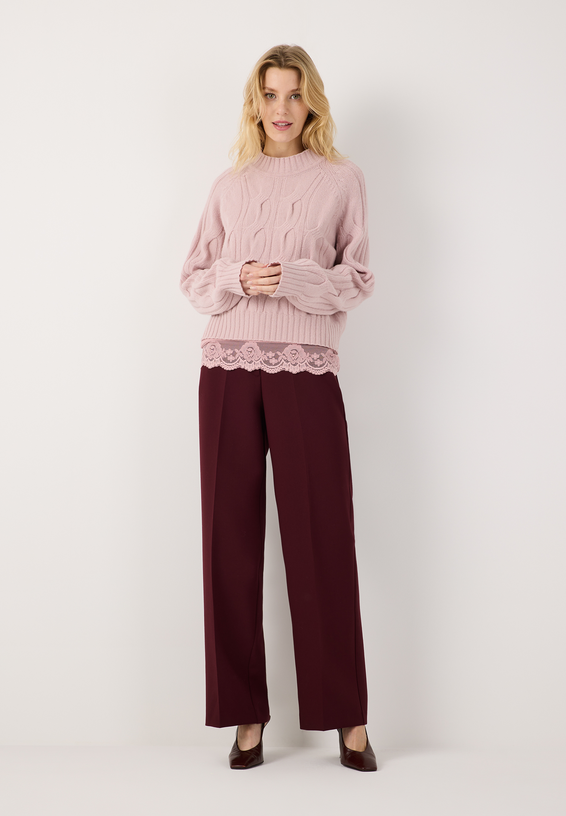 MORE & MORE Pullover in Zopfstrick, rosa, mit weinroter Hose und rosa Spitzen-Top. Model lächelt.