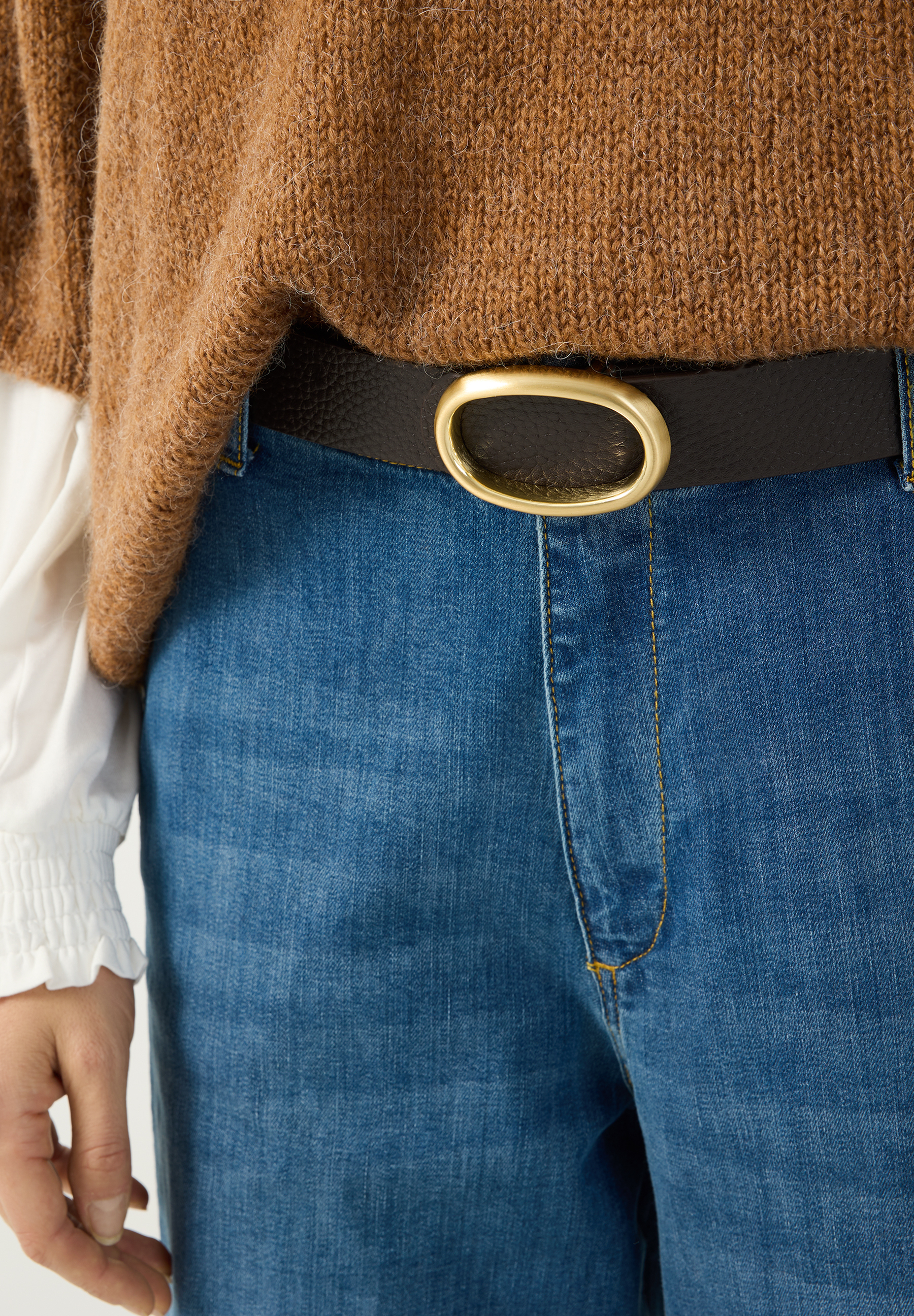 MORE & MORE Gürtel aus schwarzem Leder mit goldener ovaler Schnalle, kombiniert mit Jeans und braunem Strickpullover. MORE & MORE Gürtel aus schwarzem Leder mit goldener ovaler Schnalle, kombiniert mit Jeans und braunem Strickpullover.