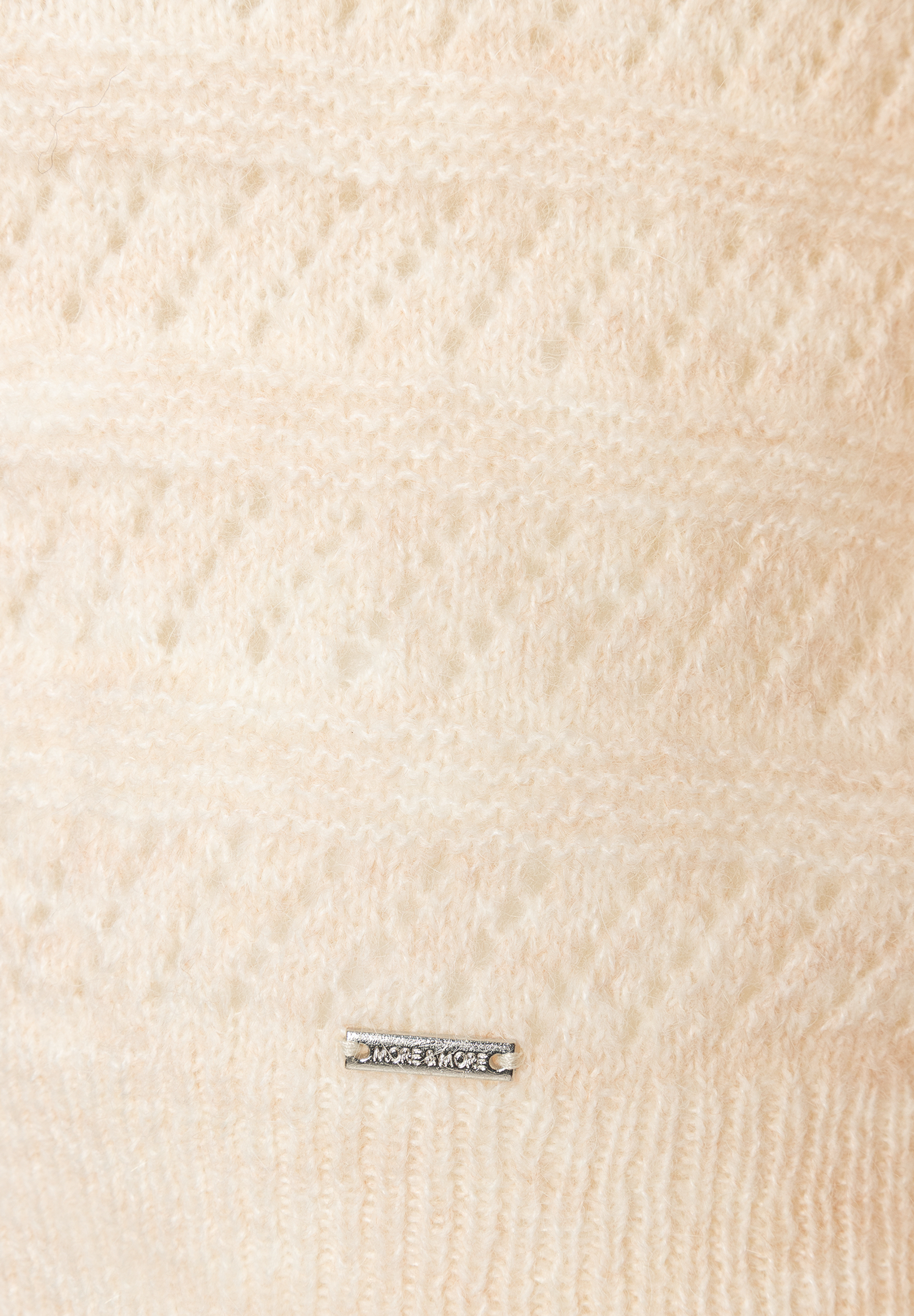MORE & MORE Pullover. Nahaufnahme beiger Strickware, die ein abstraktes Muster zeigt, mit einem silbernen Logo unten. MORE & MORE Pullover. Nahaufnahme beiger Strickware, die ein abstraktes Muster zeigt, mit einem silbernen Logo unten.