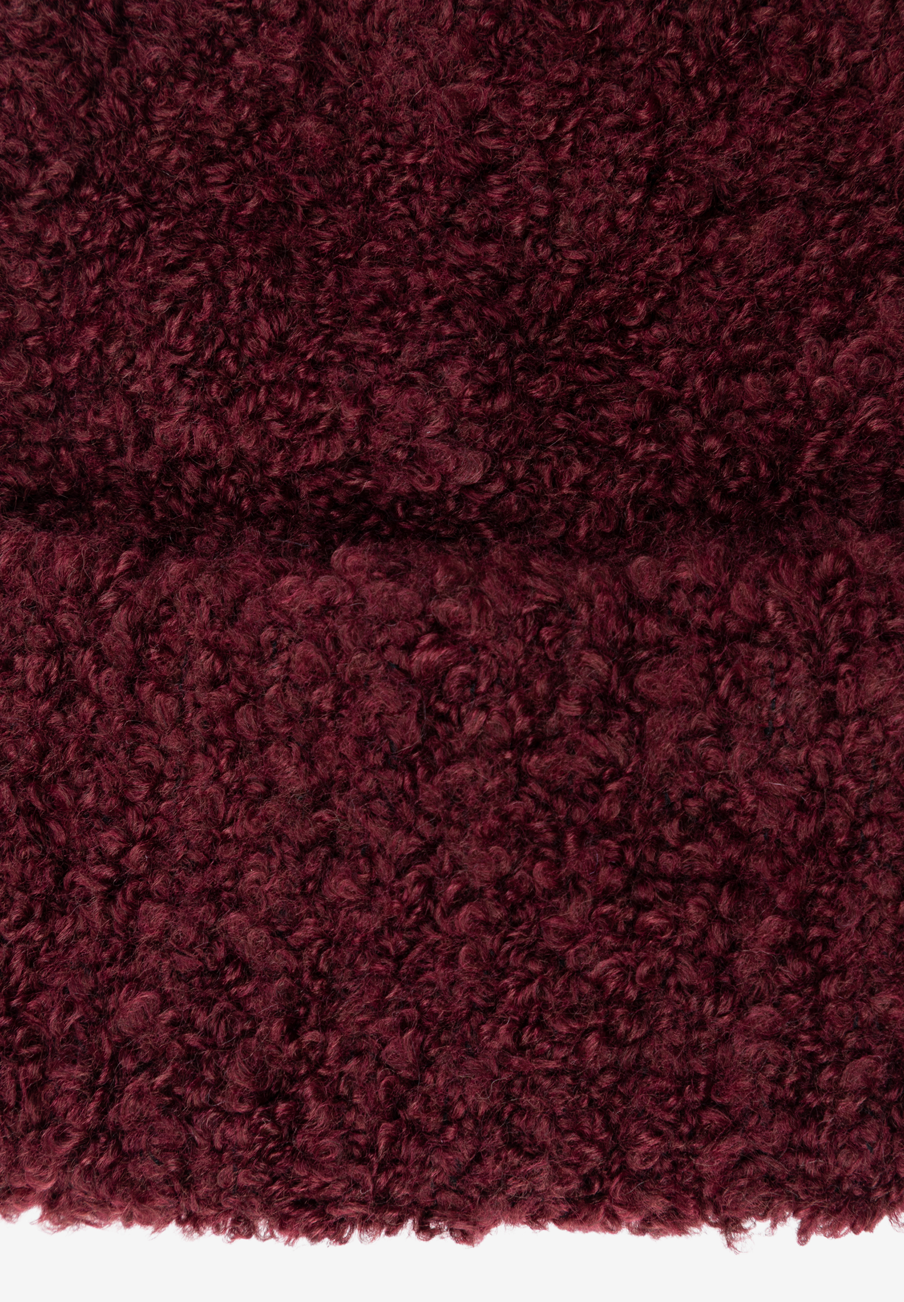 Nahaufnahme der texturierten Oberfläche eines MORE & MORE Huts/einer Mütze in tiefem Burgunderrot. Nahaufnahme der texturierten Oberfläche eines MORE & MORE Huts/einer Mütze in tiefem Burgunderrot.