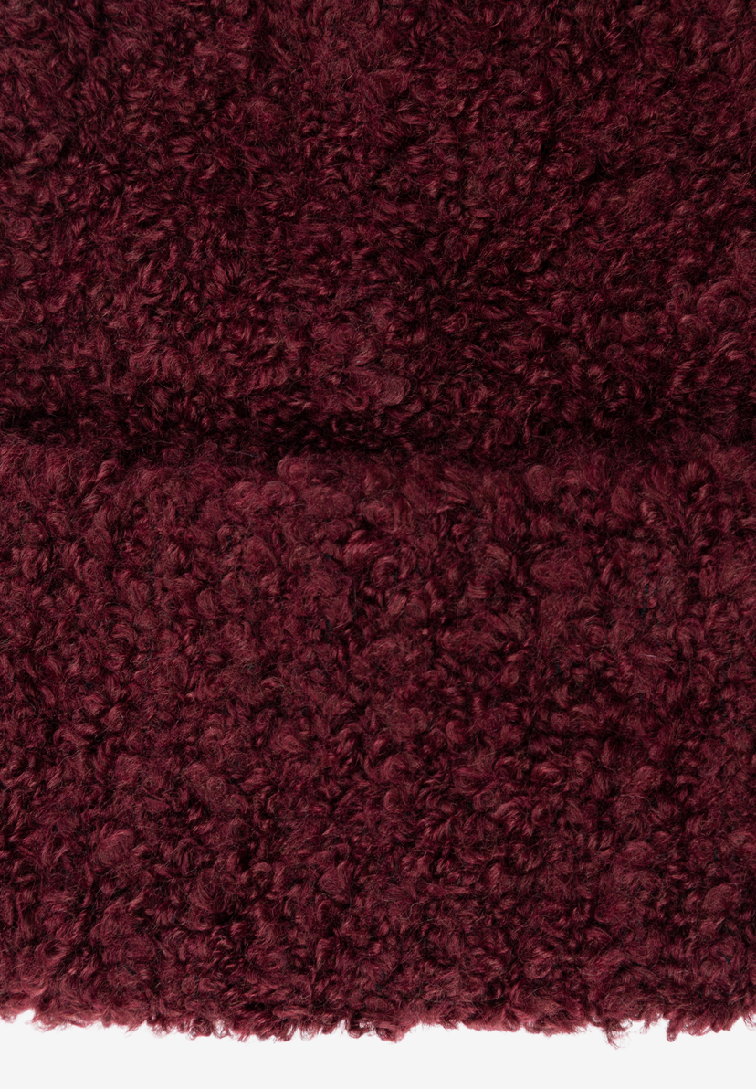 Nahaufnahme der texturierten Oberfläche eines MORE & MORE Huts/einer Mütze in tiefem Burgunderrot. Nahaufnahme der texturierten Oberfläche eines MORE & MORE Huts/einer Mütze in tiefem Burgunderrot.