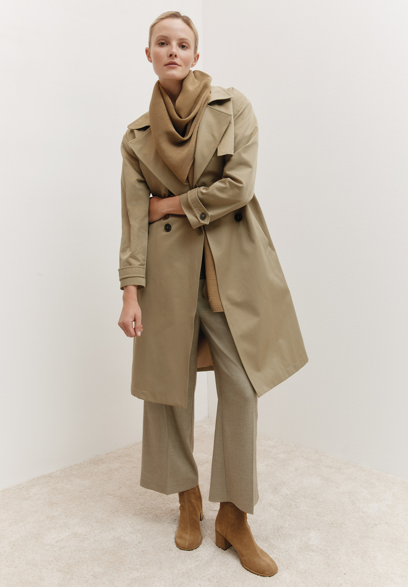 Eine Frau trägt einen MORE & MORE Trenchcoat, eine passende Hose und Stiefeletten vor einem weißen Hintergrund. Eine Frau trägt einen MORE & MORE Trenchcoat, eine passende Hose und Stiefeletten vor einem weißen Hintergrund.