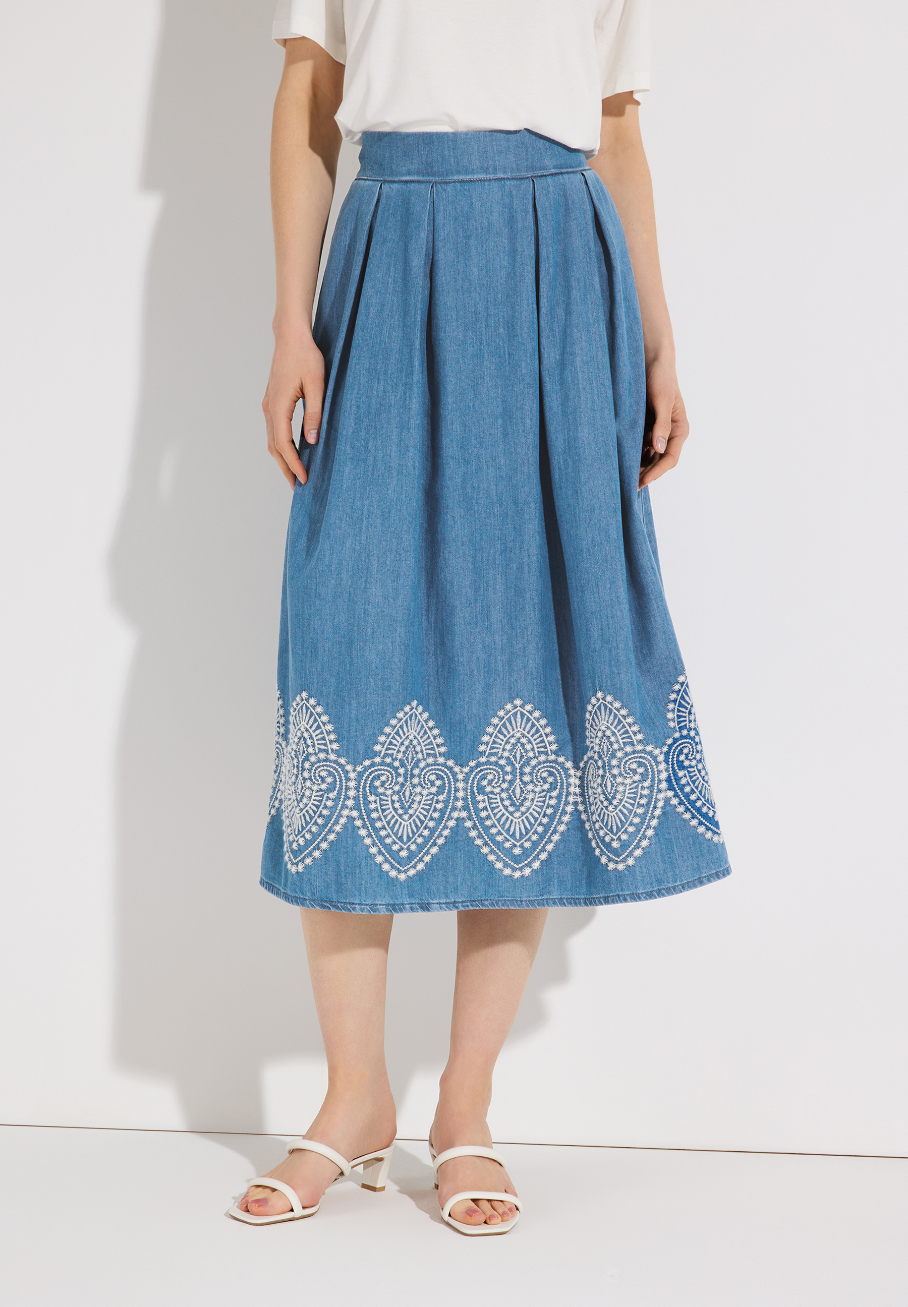 Ein MORE & MORE Jeansrock mit weißer Stickerei am Saum wird von einem Model getragen. Ein MORE & MORE Jeansrock mit weißer Stickerei am Saum wird von einem Model getragen.