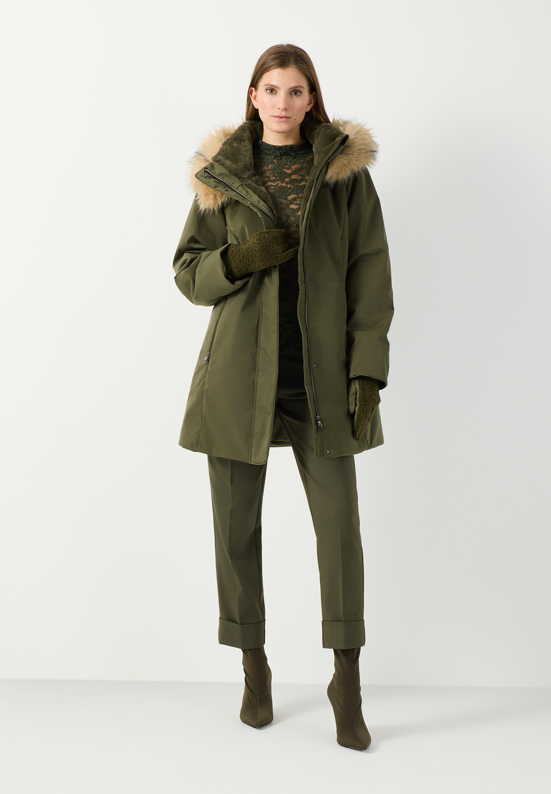 MORE & MORE Parka in Khaki, gefüttert, mit Kunstfellkragen. Darunter Strickjacke mit Rautenmuster, Jeans. Model lächelt. MORE & MORE Parka in Khaki, gefüttert, mit Kunstfellkragen. Darunter Strickjacke mit Rautenmuster, Jeans. Model lächelt.