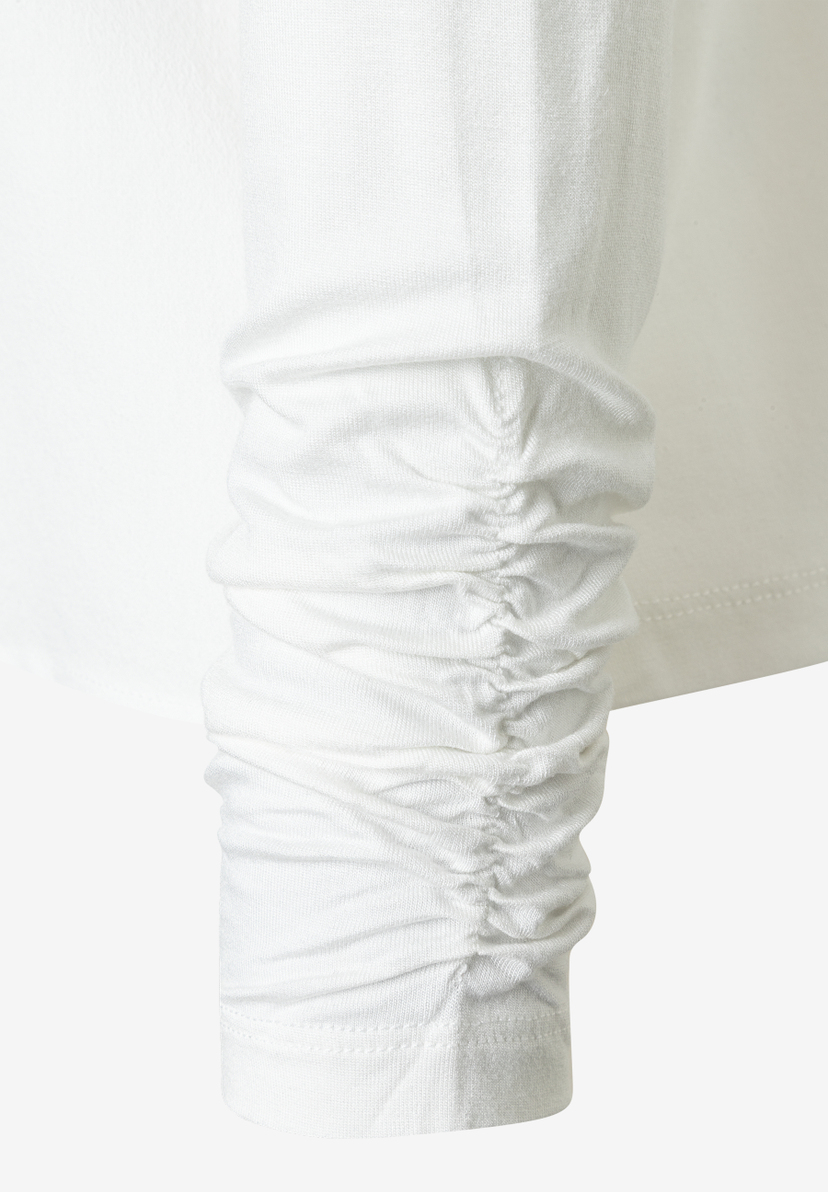 Detailaufnahme des gerafften Ärmels einer weißen MORE & MORE Bluse. Detailaufnahme des gerafften Ärmels einer weißen MORE & MORE Bluse.