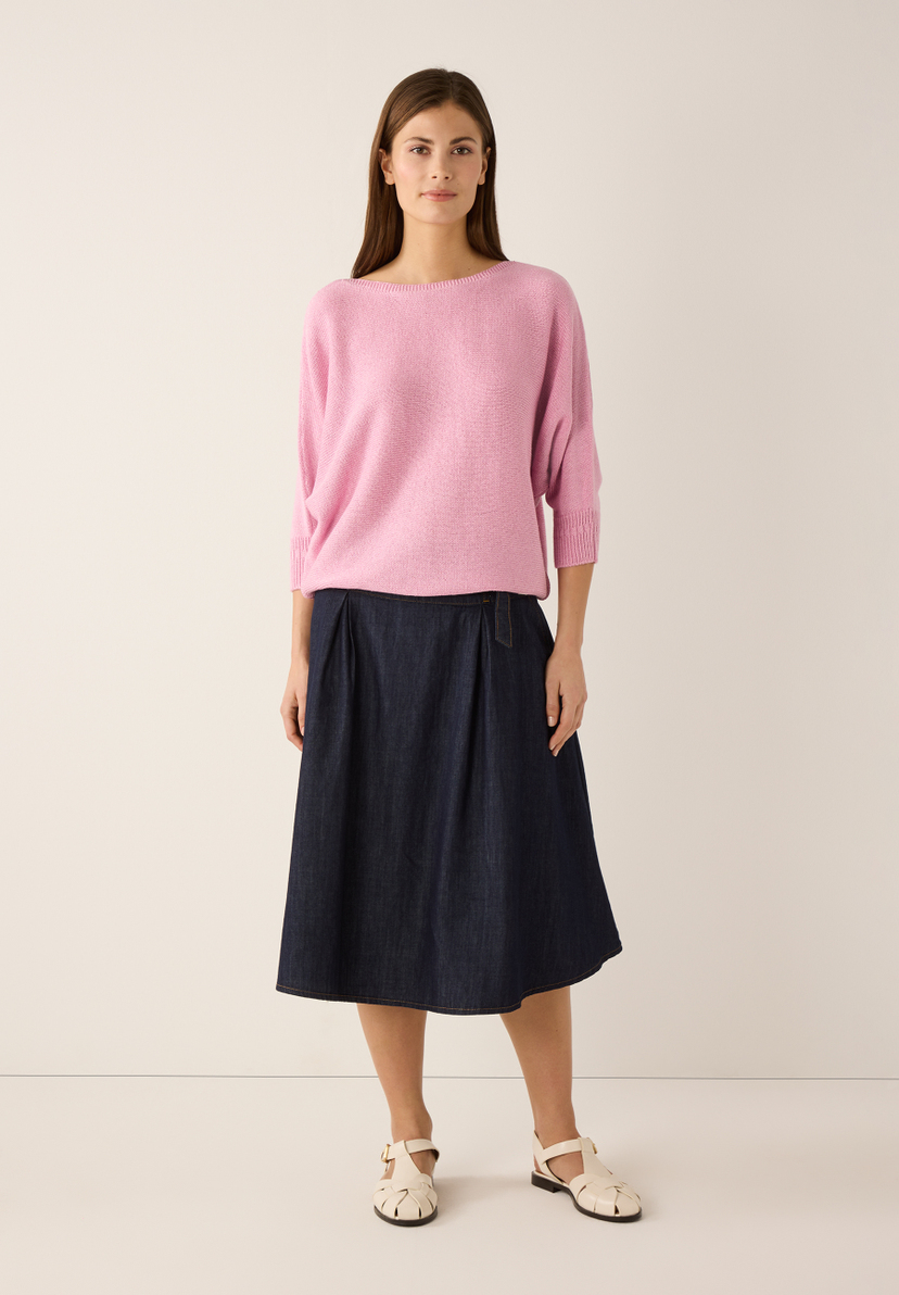 Eine Frau, die einen rosa MORE & MORE Strickpullover und einen Jeansrock trägt. Eine Frau, die einen rosa MORE & MORE Strickpullover und einen Jeansrock trägt.