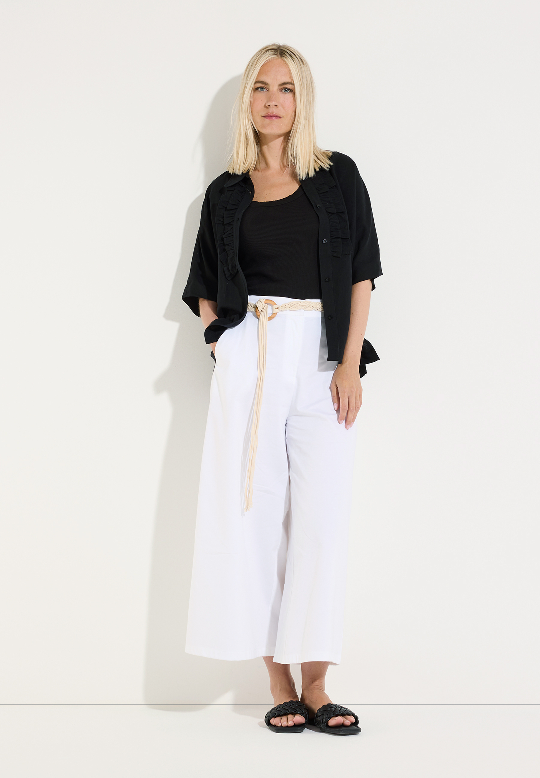 MORE & MORE Bluse: Eine blonde Frau trägt eine schwarze Kurzarm-Bluse über einem Tanktop, weiße Hosen und schwarze Sandalen. MORE & MORE Bluse: Eine blonde Frau trägt eine schwarze Kurzarm-Bluse über einem Tanktop, weiße Hosen und schwarze Sandalen.