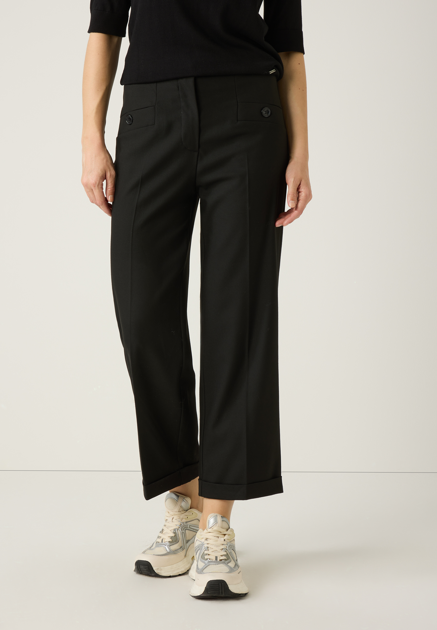 Eine Person trägt eine schwarze MORE & MORE Hose aus Viskosemischung mit Umschlag und dazu helle Turnschuhe.