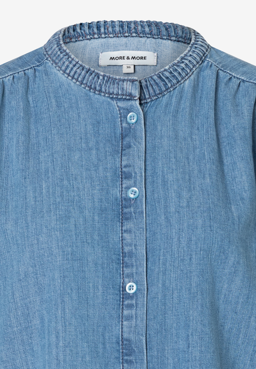 Nahaufnahme einer blauen Jeansbluse von MORE & MORE mit Knopfleiste und kleinem Stehkragen. Nahaufnahme einer blauen Jeansbluse von MORE & MORE mit Knopfleiste und kleinem Stehkragen.