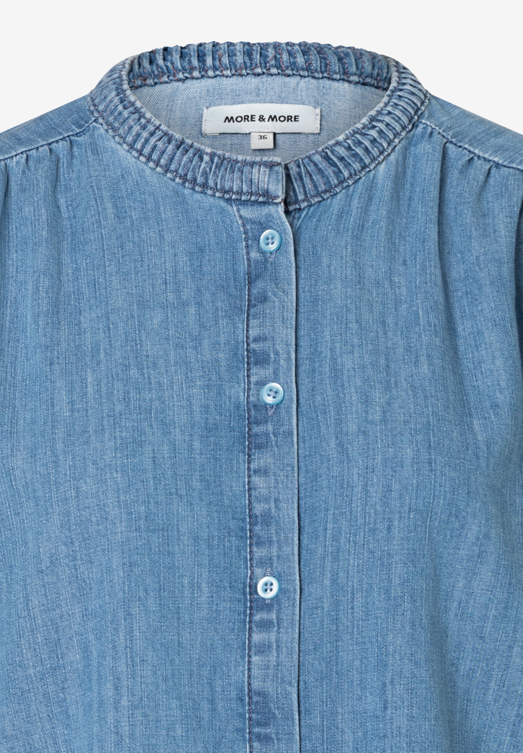 Nahaufnahme einer blauen Jeansbluse von MORE & MORE mit Knopfleiste und kleinem Stehkragen. Nahaufnahme einer blauen Jeansbluse von MORE & MORE mit Knopfleiste und kleinem Stehkragen.