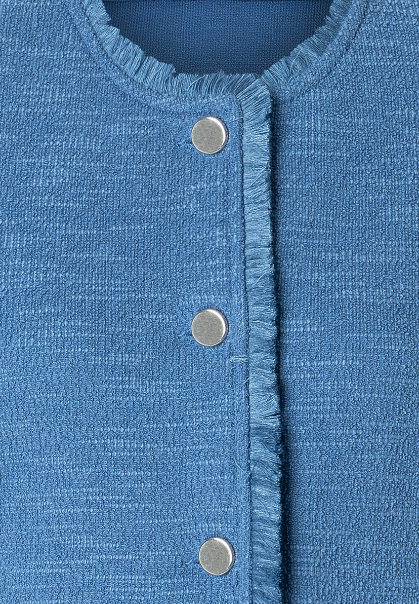 Nahaufnahme eines blauen MORE & MORE Blazers mit Bouclé-Textur und silbernen Knöpfen. Nahaufnahme eines blauen MORE & MORE Blazers mit Bouclé-Textur und silbernen Knöpfen.