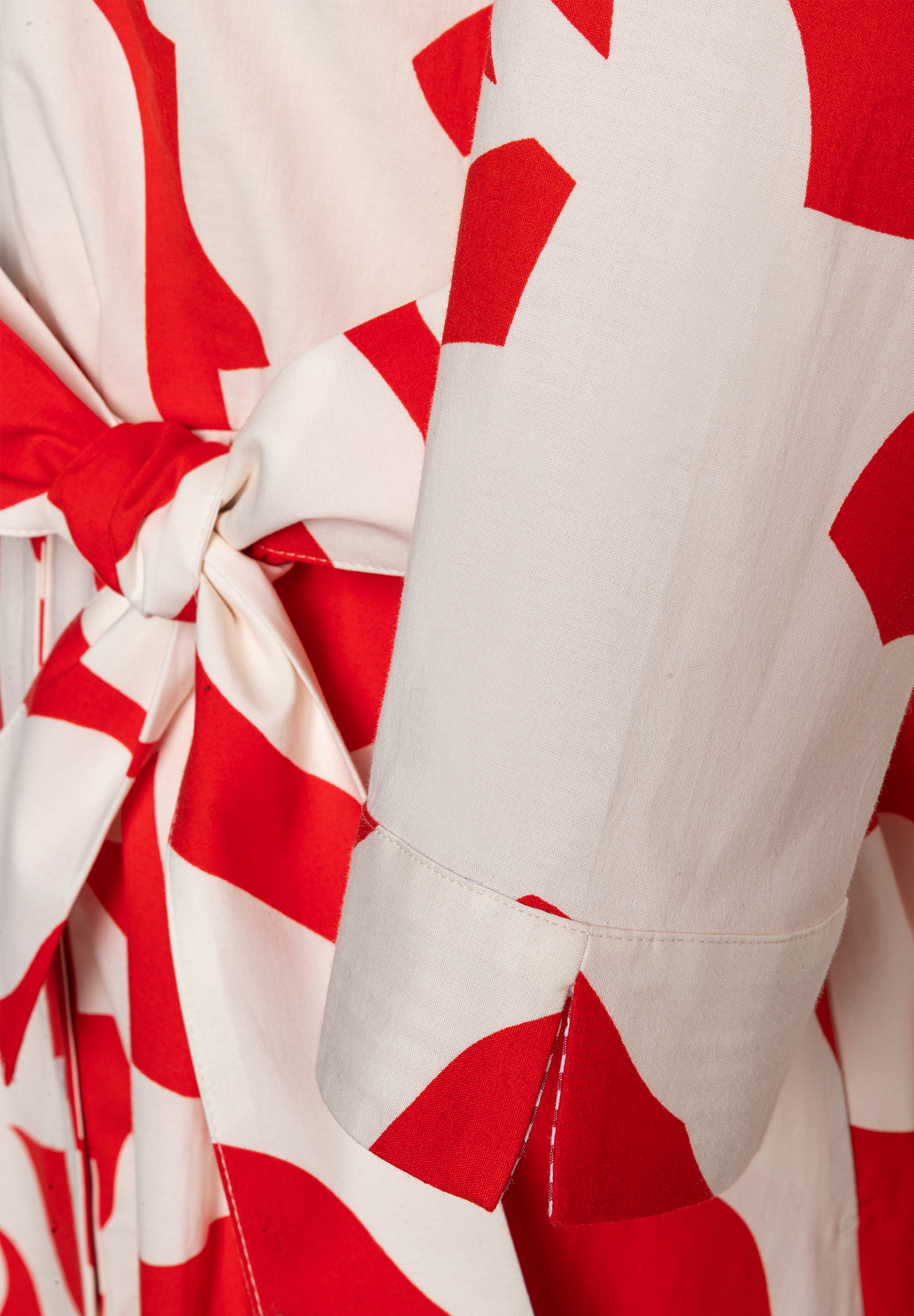 Detailansicht eines MORE & MORE Oberteils mit weiß-rotem Muster und Bindegürtel. Detailansicht eines MORE & MORE Oberteils mit weiß-rotem Muster und Bindegürtel.