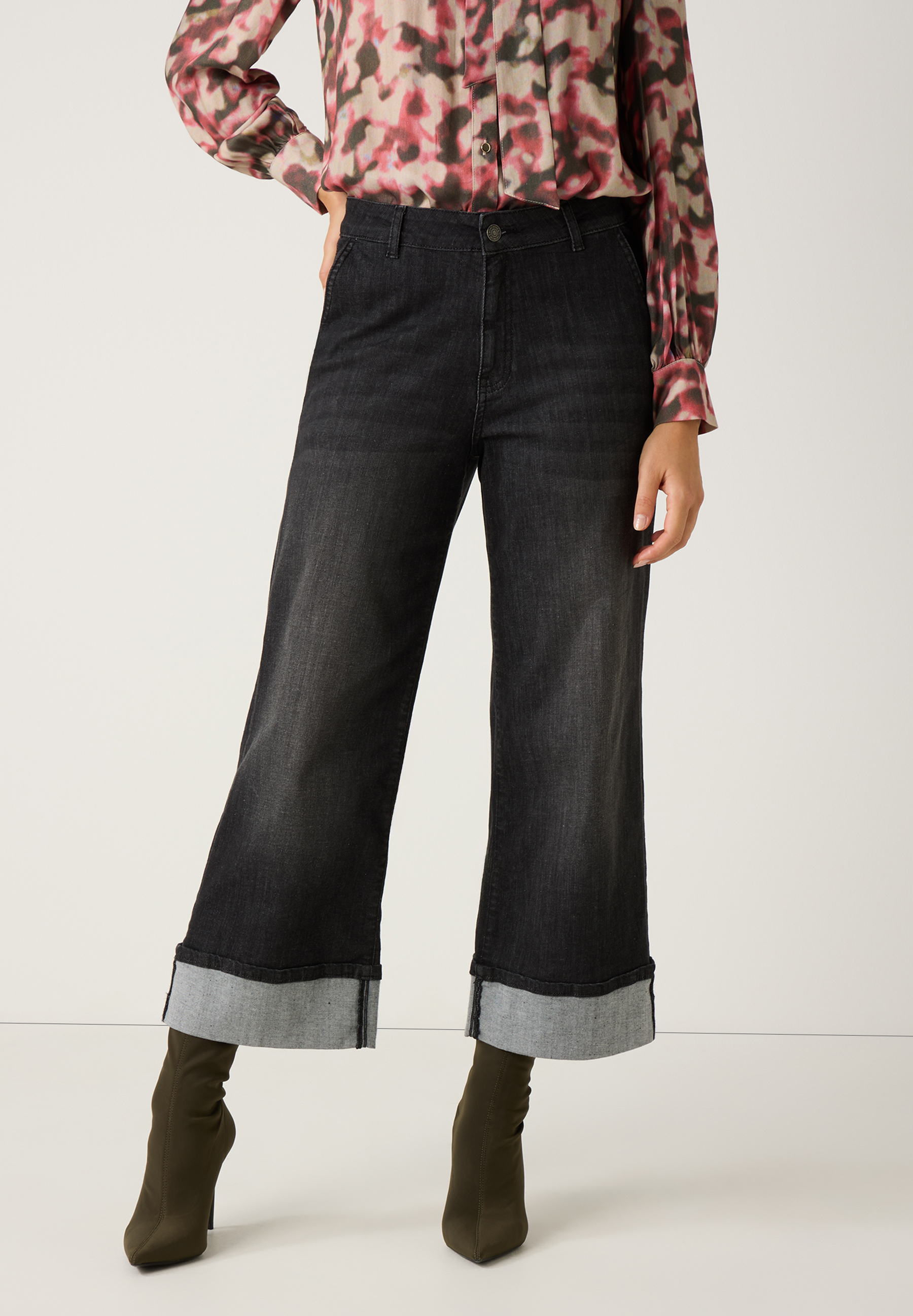 Eine MORE & MORE Jeans aus Denim mit weitem Bein und hochgekrempeltem Saum, kombiniert mit olivgrünen Stiefeln.
