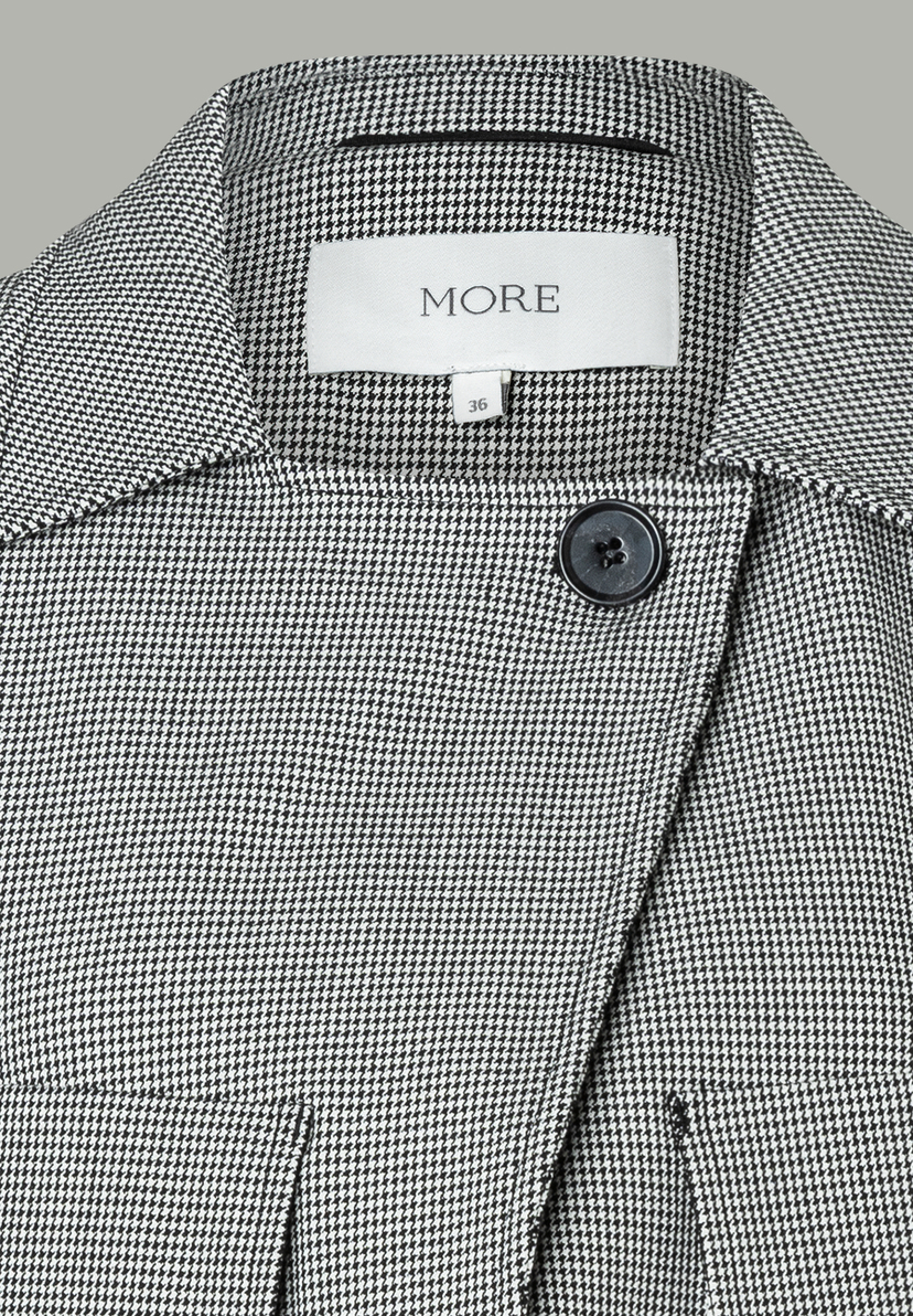 Nahaufnahme eines MORE & MORE Oberteils mit Hahnentrittmuster und Knopf. Nahaufnahme eines MORE & MORE Oberteils mit Hahnentrittmuster und Knopf.