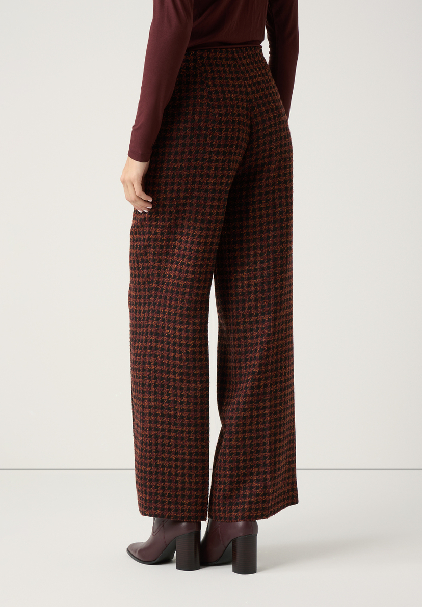 Eine Frau trägt eine braun-schwarz gemusterte Bouclé-Hose von MORE & MORE und dazu passende Stiefeletten. Eine Frau trägt eine braun-schwarz gemusterte Bouclé-Hose von MORE & MORE und dazu passende Stiefeletten.