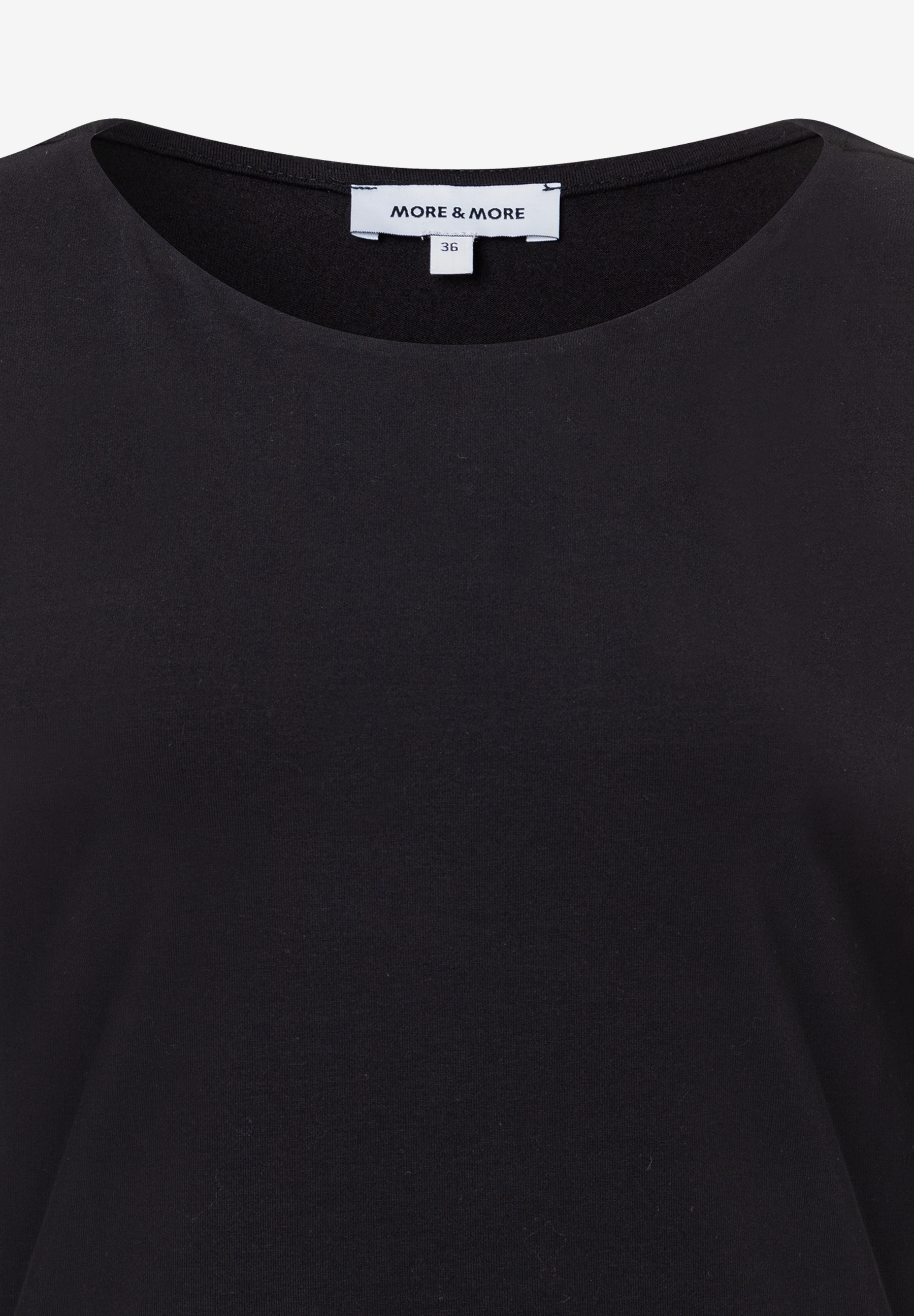 Nahaufnahme eines schwarzen MORE & MORE Oberteils aus Jersey mit angenehmem Tragekomfort und einem Etikett mit der Größe 36. Nahaufnahme eines schwarzen MORE & MORE Oberteils aus Jersey mit angenehmem Tragekomfort und einem Etikett mit der Größe 36.