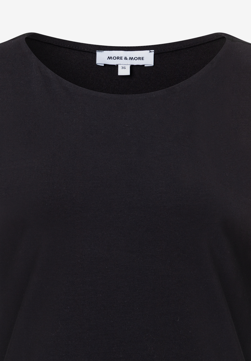 Nahaufnahme eines schwarzen MORE & MORE Oberteils aus Jersey mit angenehmem Tragekomfort und einem Etikett mit der Größe 36. Nahaufnahme eines schwarzen MORE & MORE Oberteils aus Jersey mit angenehmem Tragekomfort und einem Etikett mit der Größe 36.