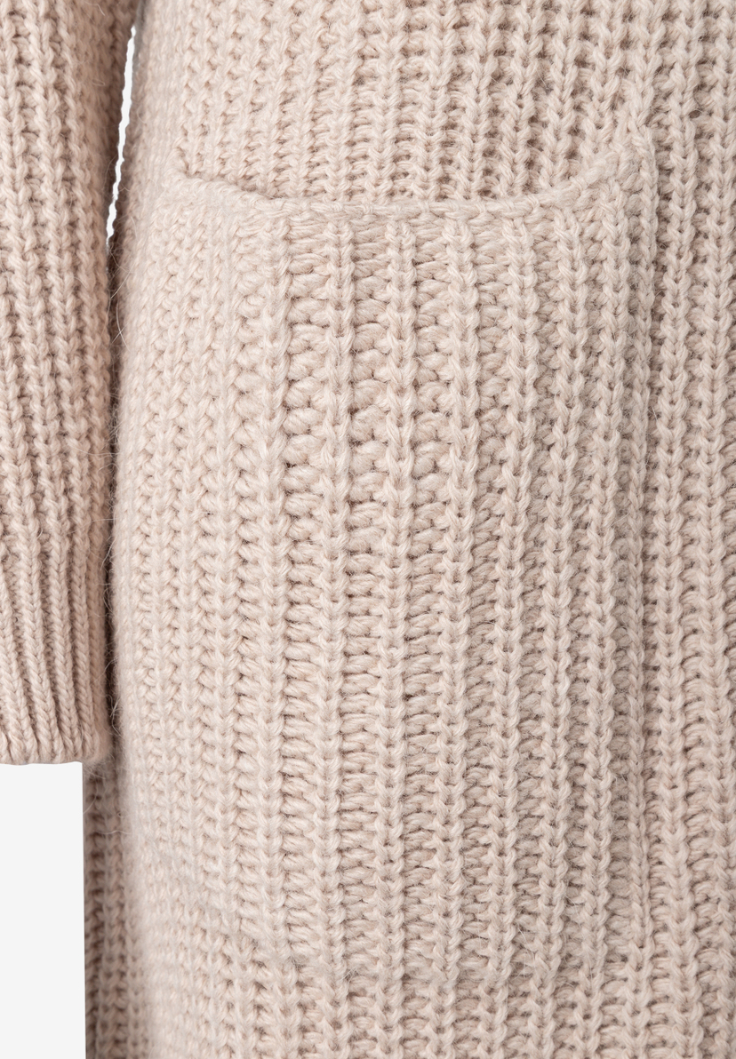 MORE & MORE Pullover & Strickwaren. Detailaufnahme eines beigen Grobstrickpullovers mit Rippenbündchen und aufgesetzter Tasche.