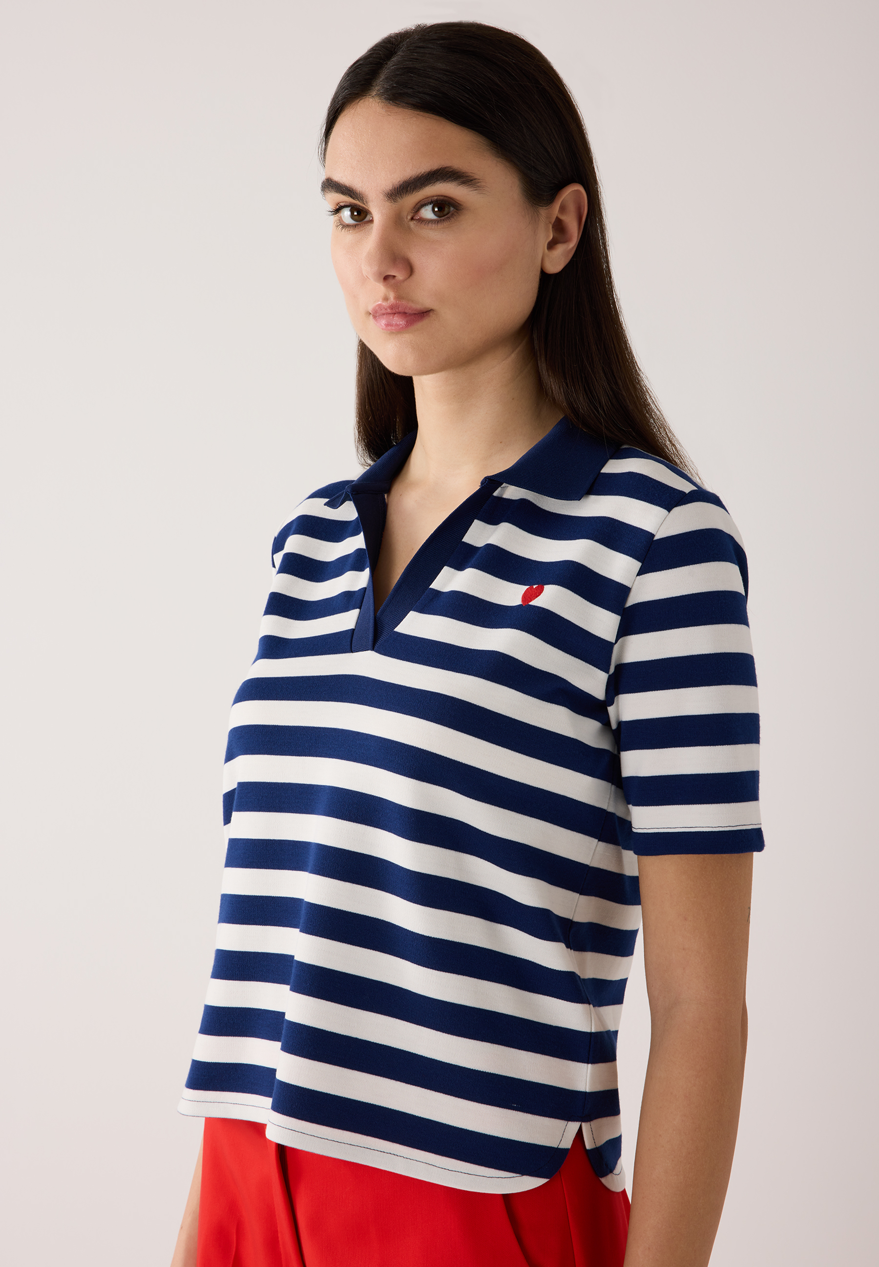 Eine Frau trägt ein gestreiftes Jersey-Poloshirt von MORE & MORE mit rotem Detail. Eine Frau trägt ein gestreiftes Jersey-Poloshirt von MORE & MORE mit rotem Detail.