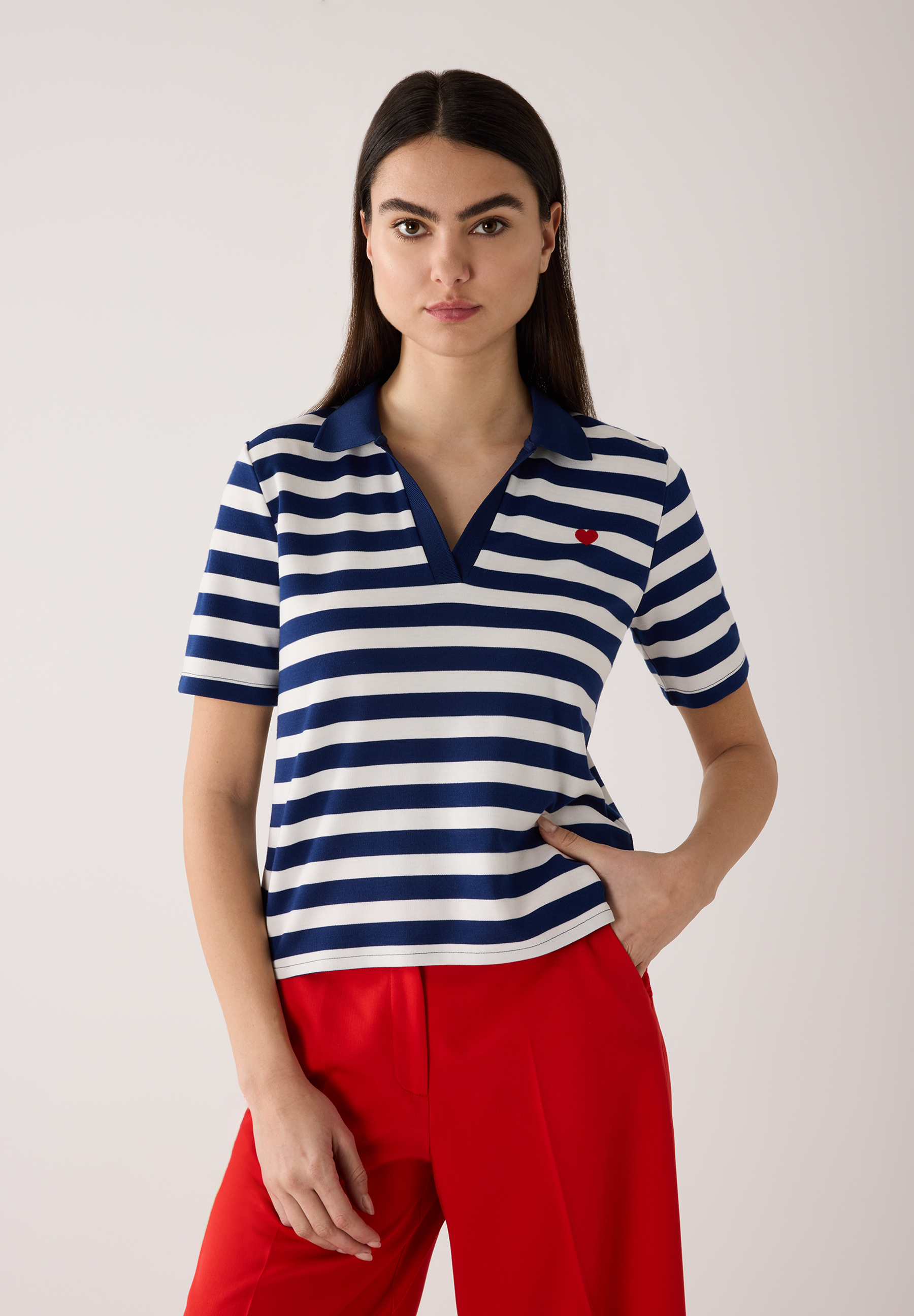 Eine Frau mit MORE & MORE Oberteil (blau-weiß gestreift) und roter Hose, die mit einer Hand in der Hosentasche posiert. Eine Frau mit MORE & MORE Oberteil (blau-weiß gestreift) und roter Hose, die mit einer Hand in der Hosentasche posiert.