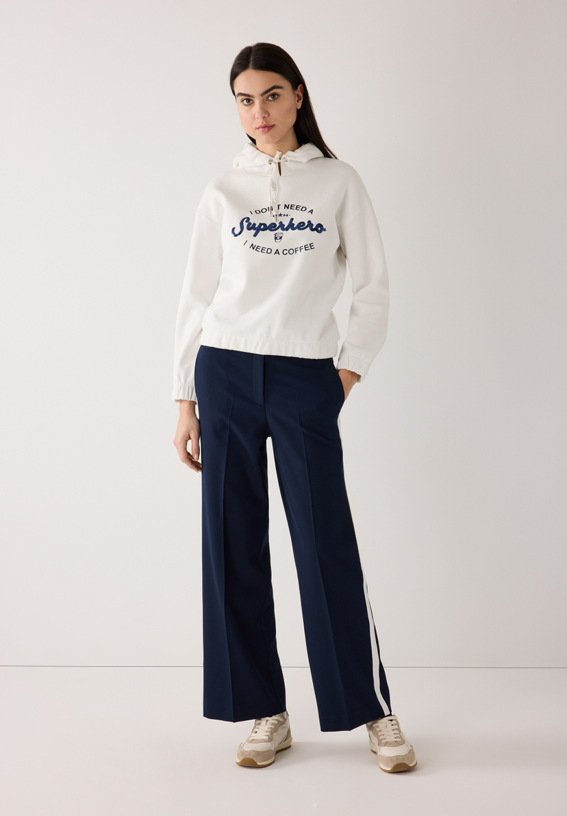 Eine Frau trägt ein MORE & MORE Sweatshirt mit Kapuze und dunkelblaue Hosen. Eine Frau trägt ein MORE & MORE Sweatshirt mit Kapuze und dunkelblaue Hosen.