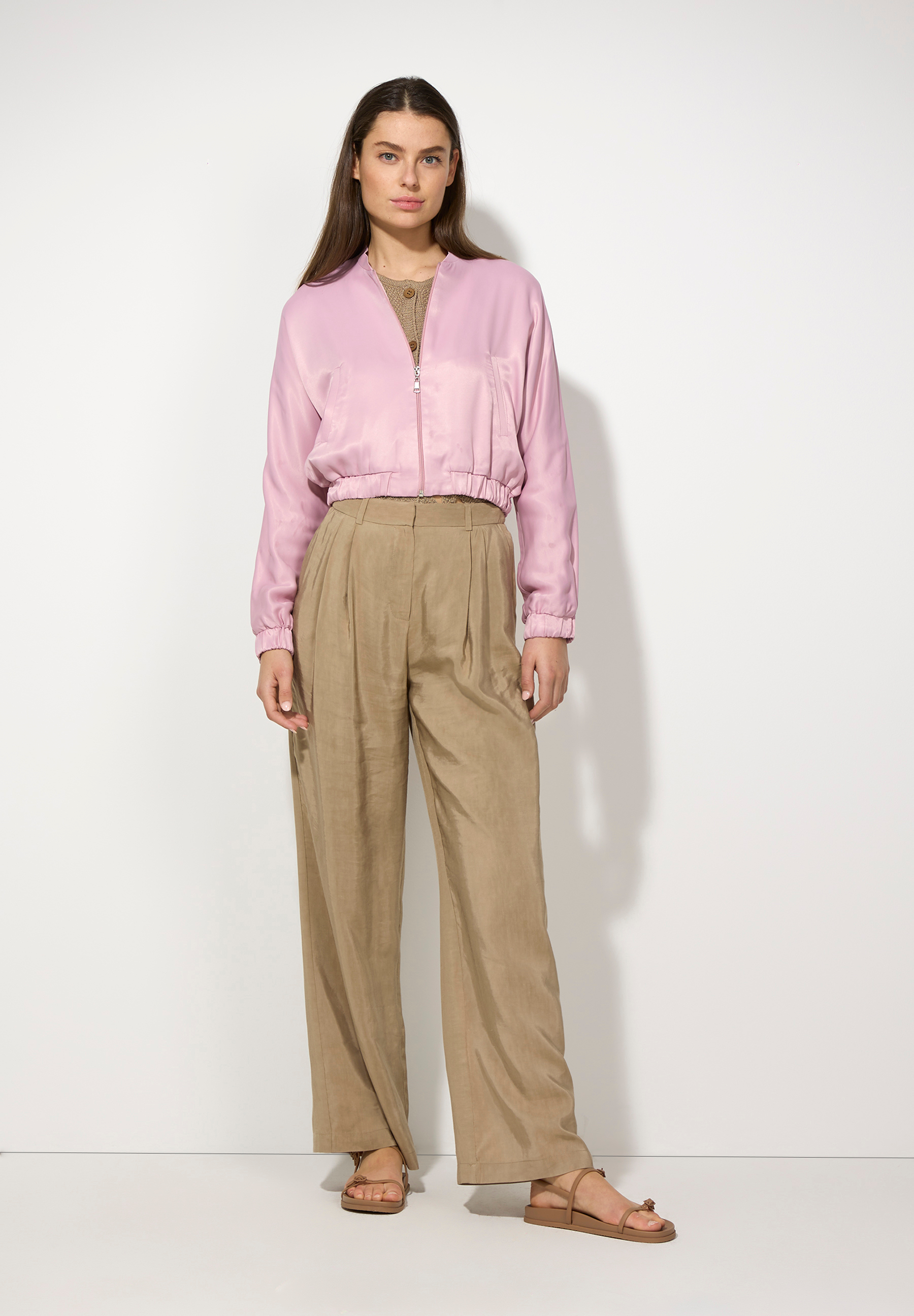 Eine Frau in MORE & MORE Oberteilen aus Satin und beigen Hosen vor einem weißen Hintergrund. Eine Frau in MORE & MORE Oberteilen aus Satin und beigen Hosen vor einem weißen Hintergrund.