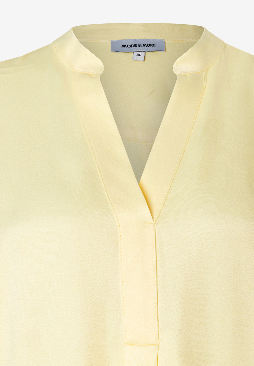 Detailaufnahme einer gelben MORE & MORE Bluse mit V-Ausschnitt und Kragen. Das Material ist glatt und glänzend. Detailaufnahme einer gelben MORE & MORE Bluse mit V-Ausschnitt und Kragen. Das Material ist glatt und glänzend.