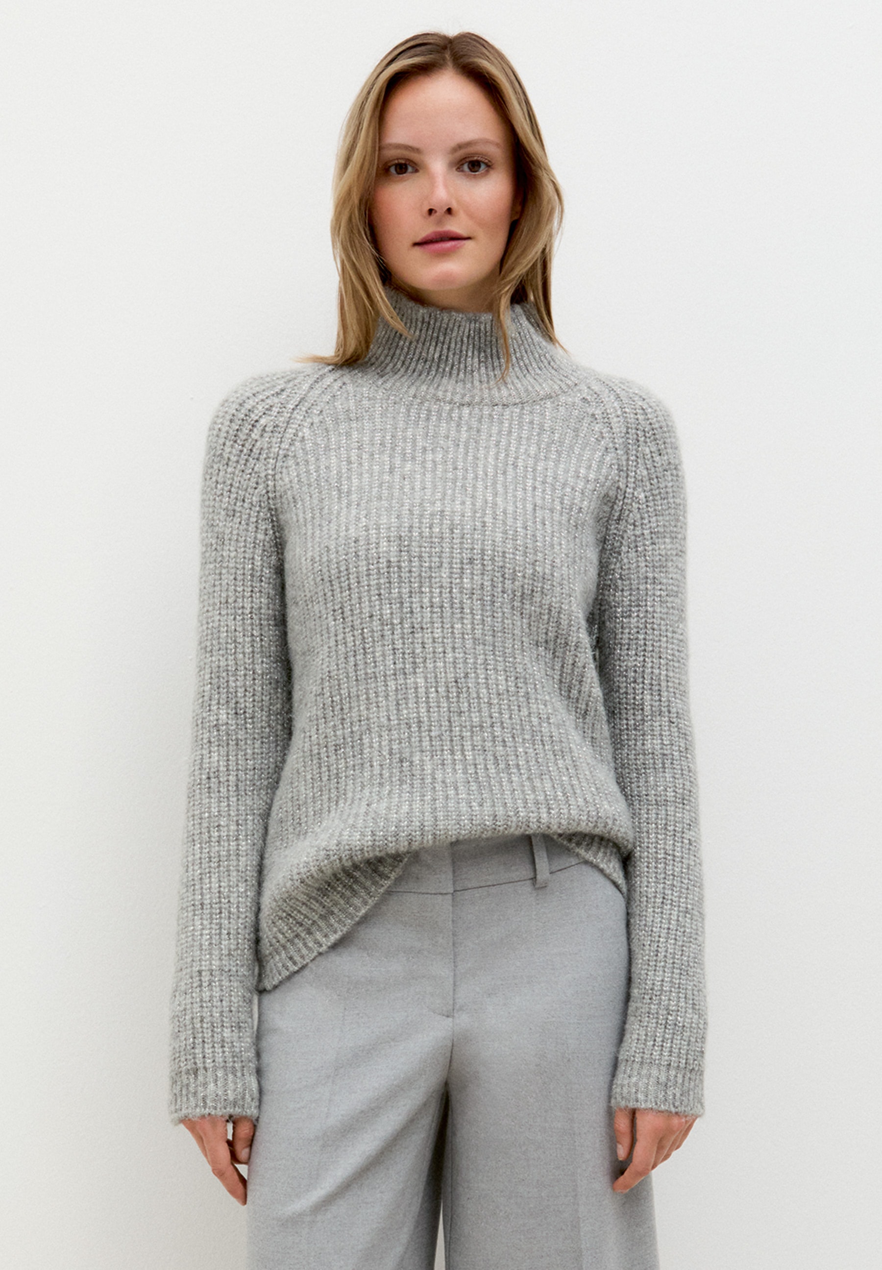 Eine Frau trägt einen grauen MORE & MORE Strickpullover, kombiniert mit einer grauen Hose vor einem weißen Hintergrund. Eine Frau trägt einen grauen MORE & MORE Strickpullover, kombiniert mit einer grauen Hose vor einem weißen Hintergrund.
