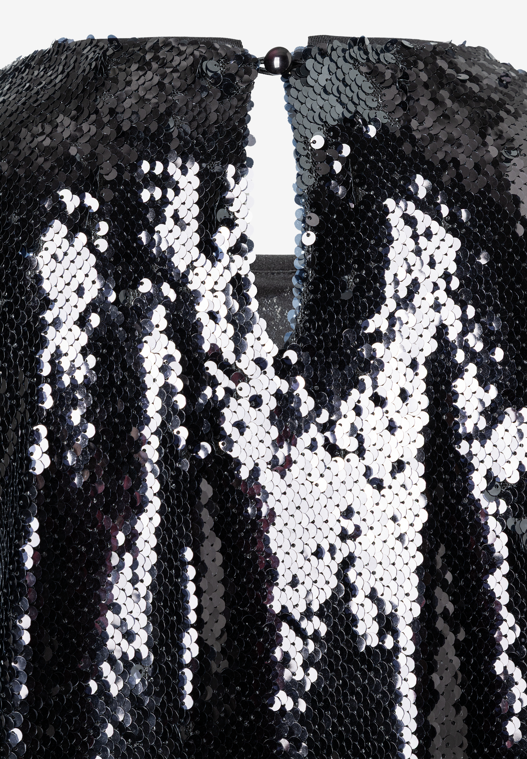 Nahaufnahme eines paillettenbesetzten MORE & MORE Oberteils. Blick auf Ausschnitt mit Knopf im Nacken. Nahaufnahme eines paillettenbesetzten MORE & MORE Oberteils. Blick auf Ausschnitt mit Knopf im Nacken.